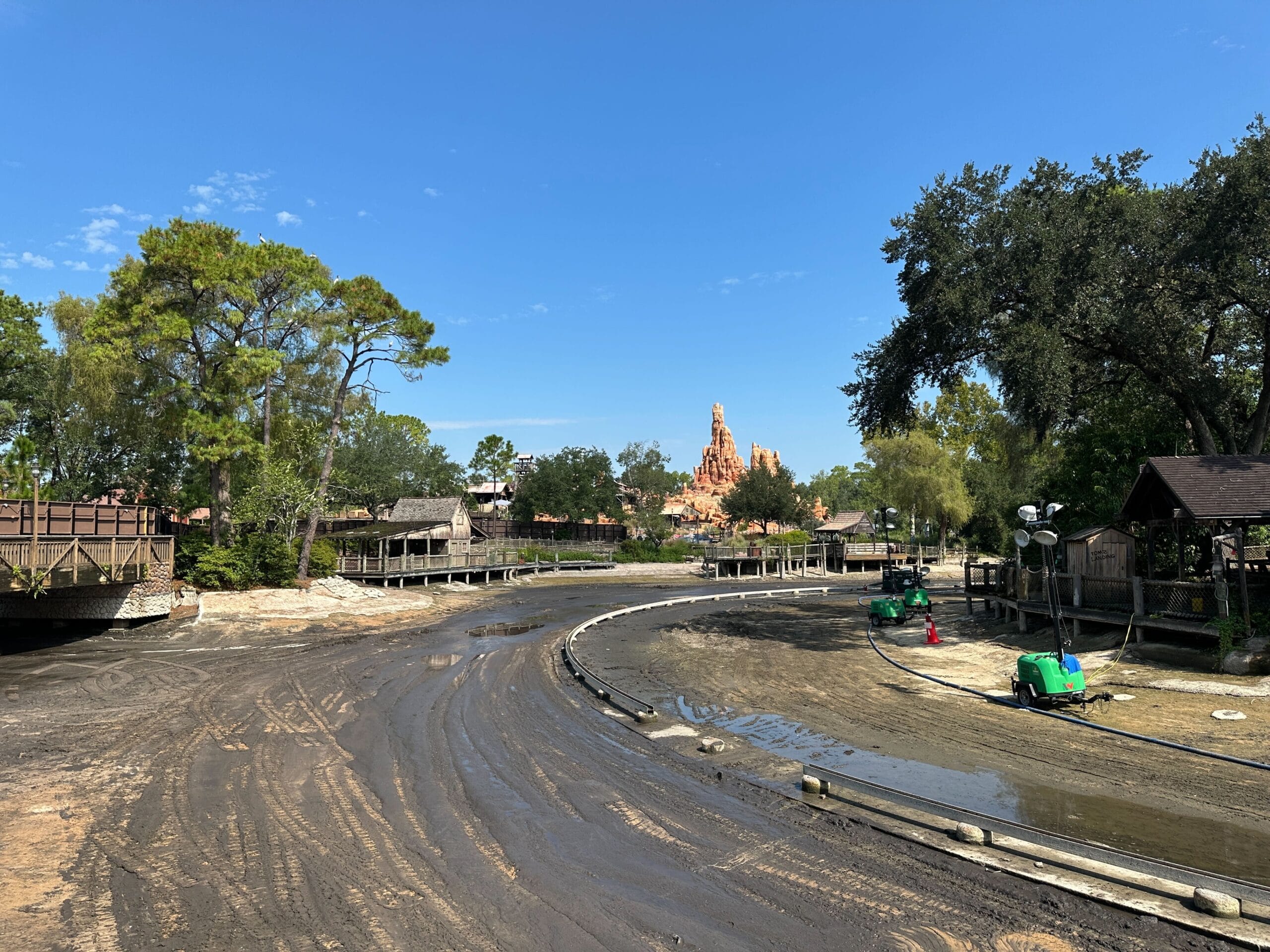 A drained Rivers of America waterway with muddy ground and a rocky mountain at Disney World under a blue sky.