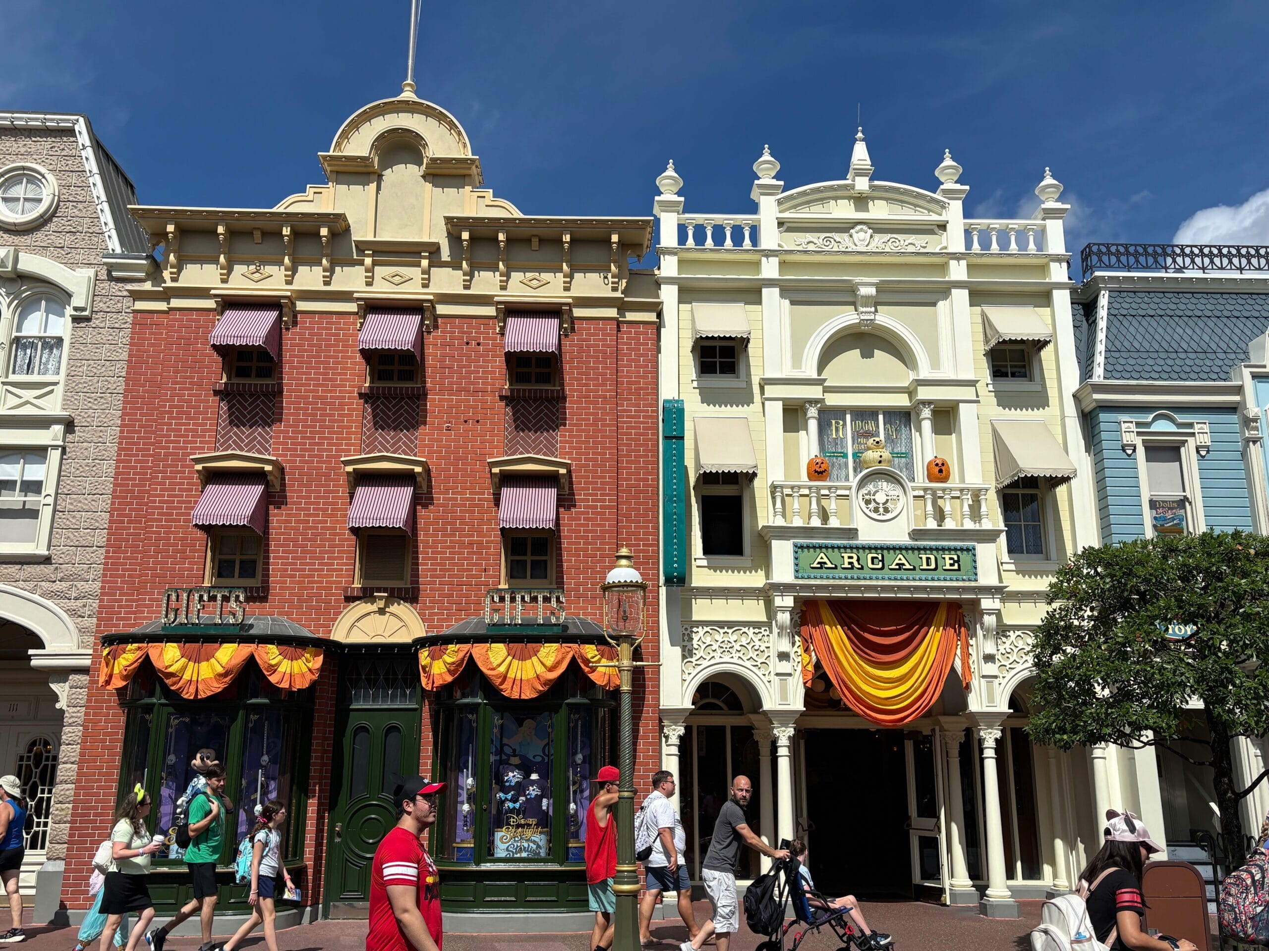 Main Street shines with Halloween Decor and banners as people stroll under a clear blue sky at Magic Kingdom.