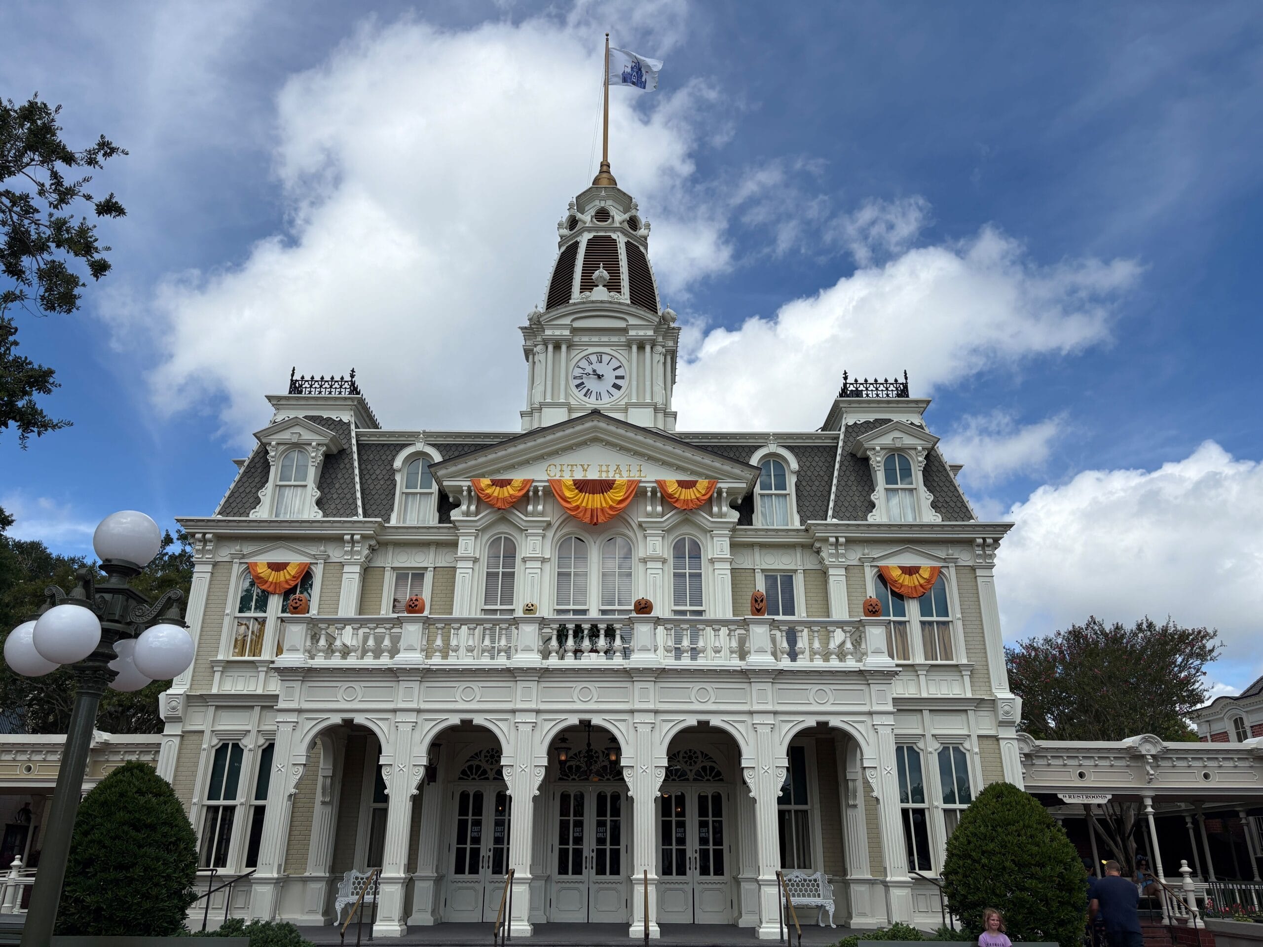 Victorian-style city hall with Halloween Decor and a clock tower in Magic Kingdom under a partly cloudy sky.