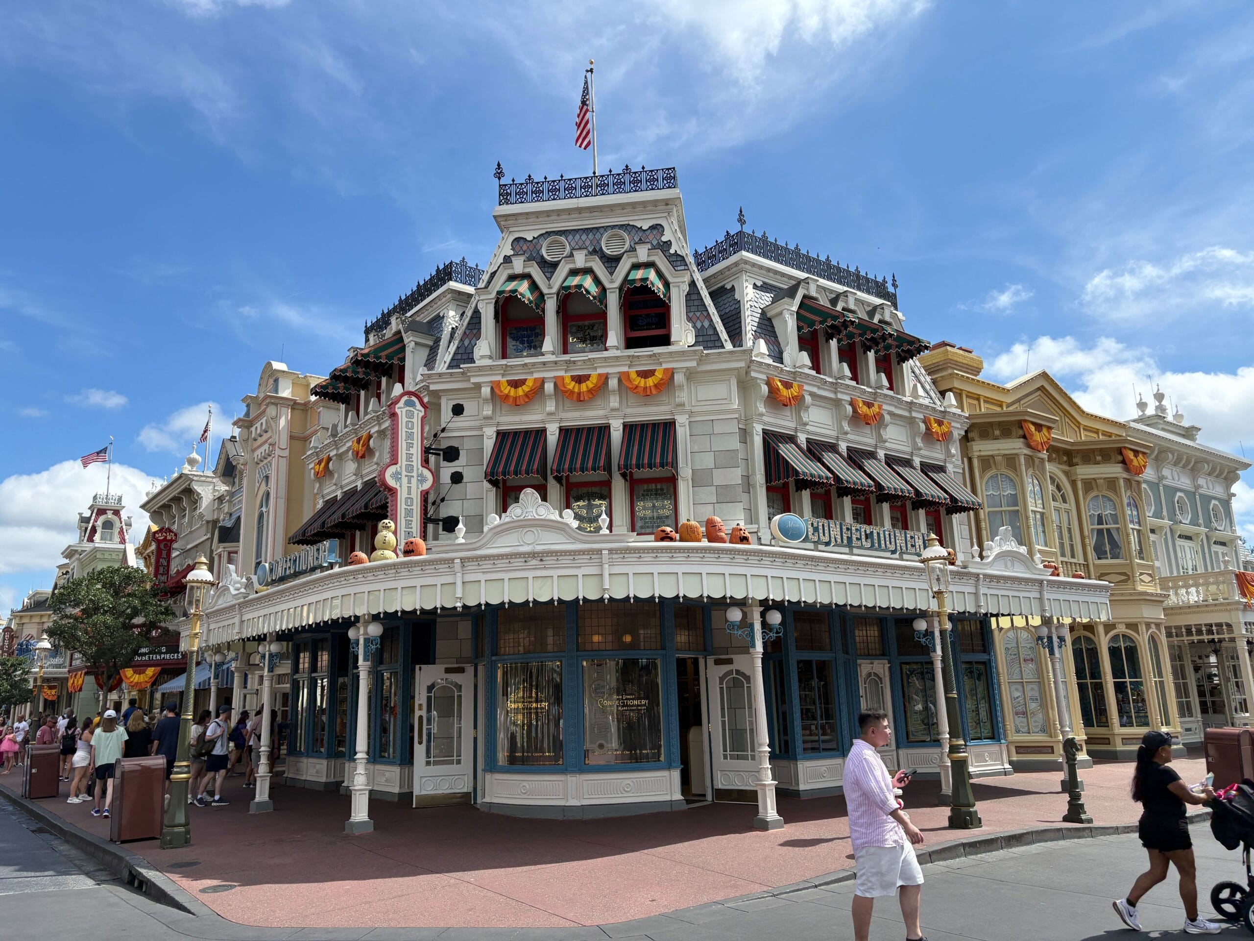 Victorian-style building with Halloween Decor at Magic Kingdom, pumpkins and orange garlands under a bright blue sky.