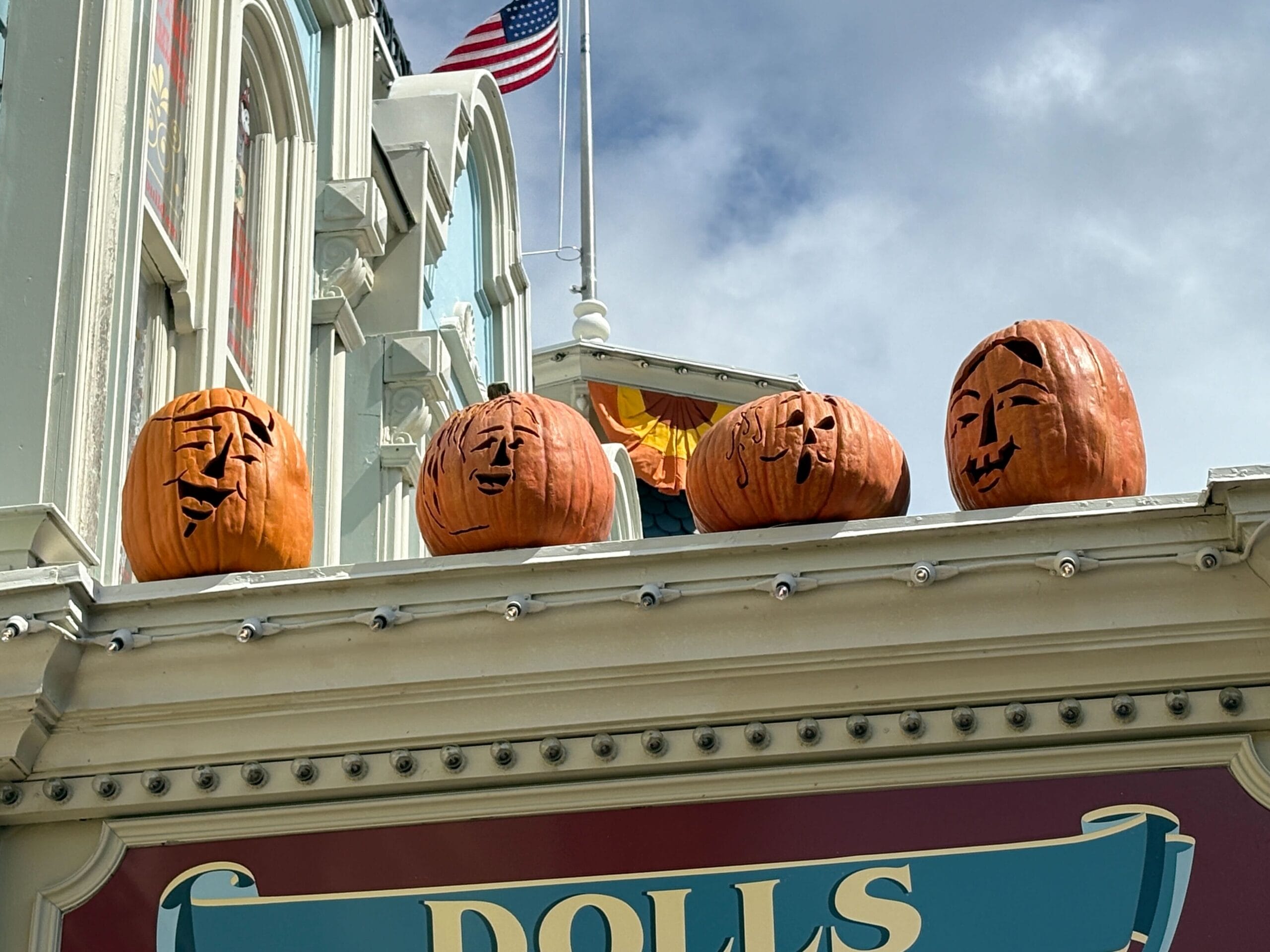 Four carved pumpkins with unique faces sit on a ledge, adding Halloween Decor to the scene against a cloudy Magic Kingdom sky.