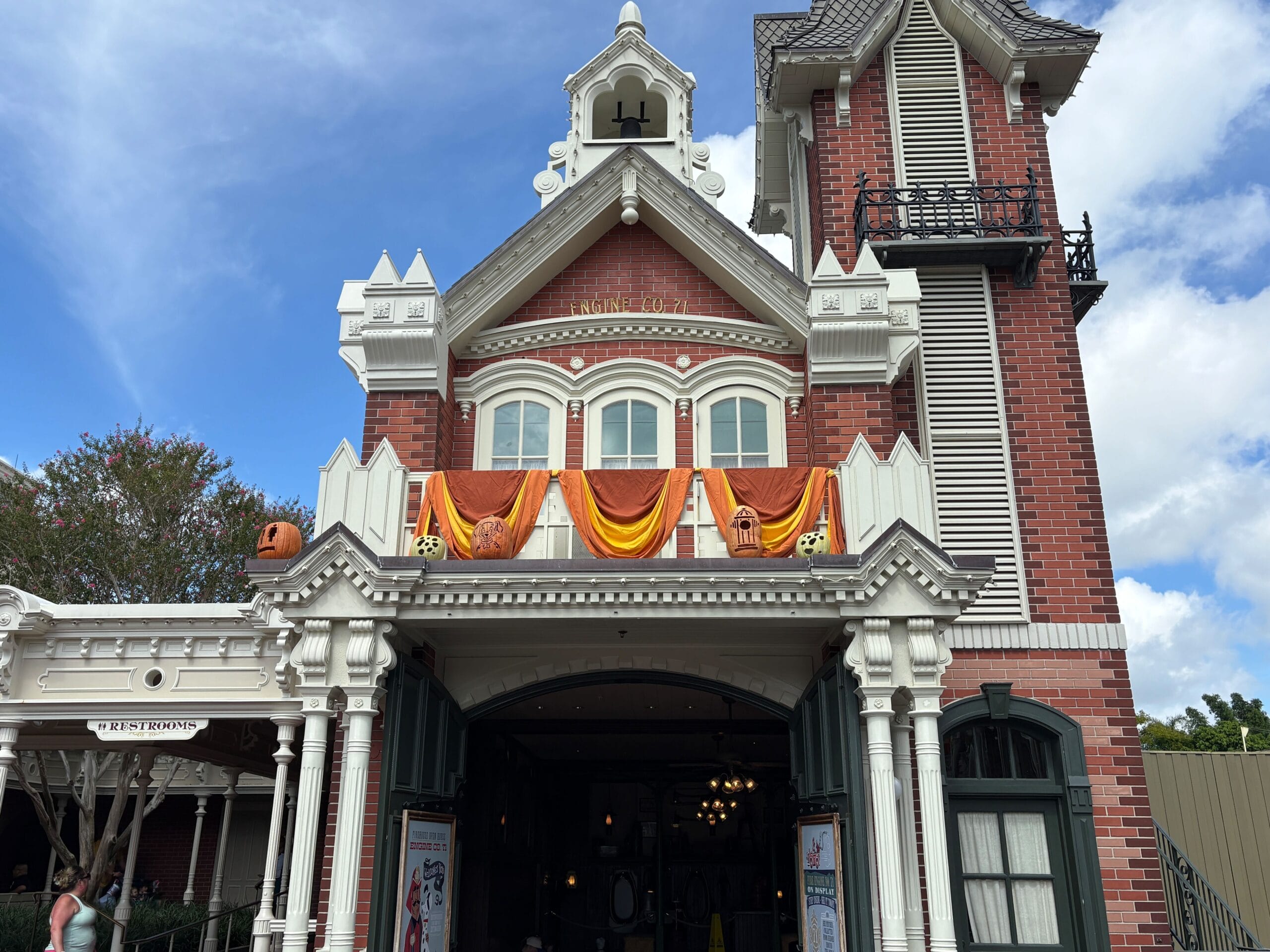 A red brick building with Halloween Decor and jack-o’-lanterns at Magic Kingdom under a blue sky.