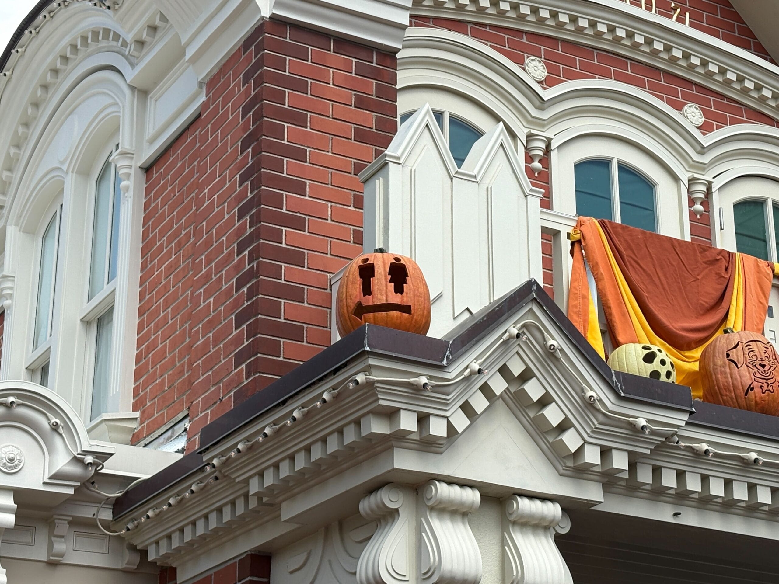 A carved pumpkin with a surprised face sits on a building ledge, adding festive Halloween decor to Magic Kingdom.