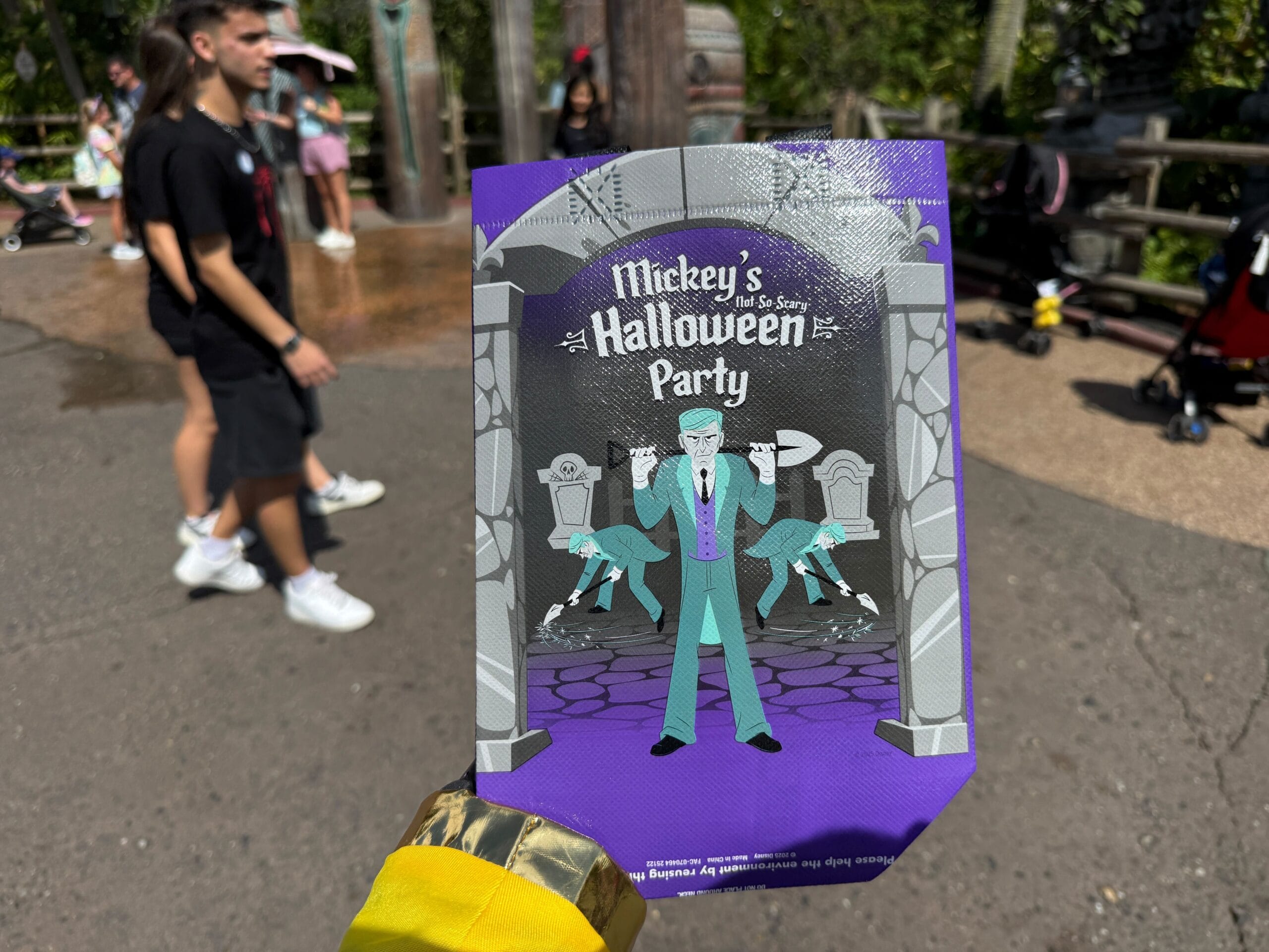 A hand holds a 2025 Mickey's Not So Scary Halloween Party treat bag and pamphlet with a villain graphic at a theme park.
