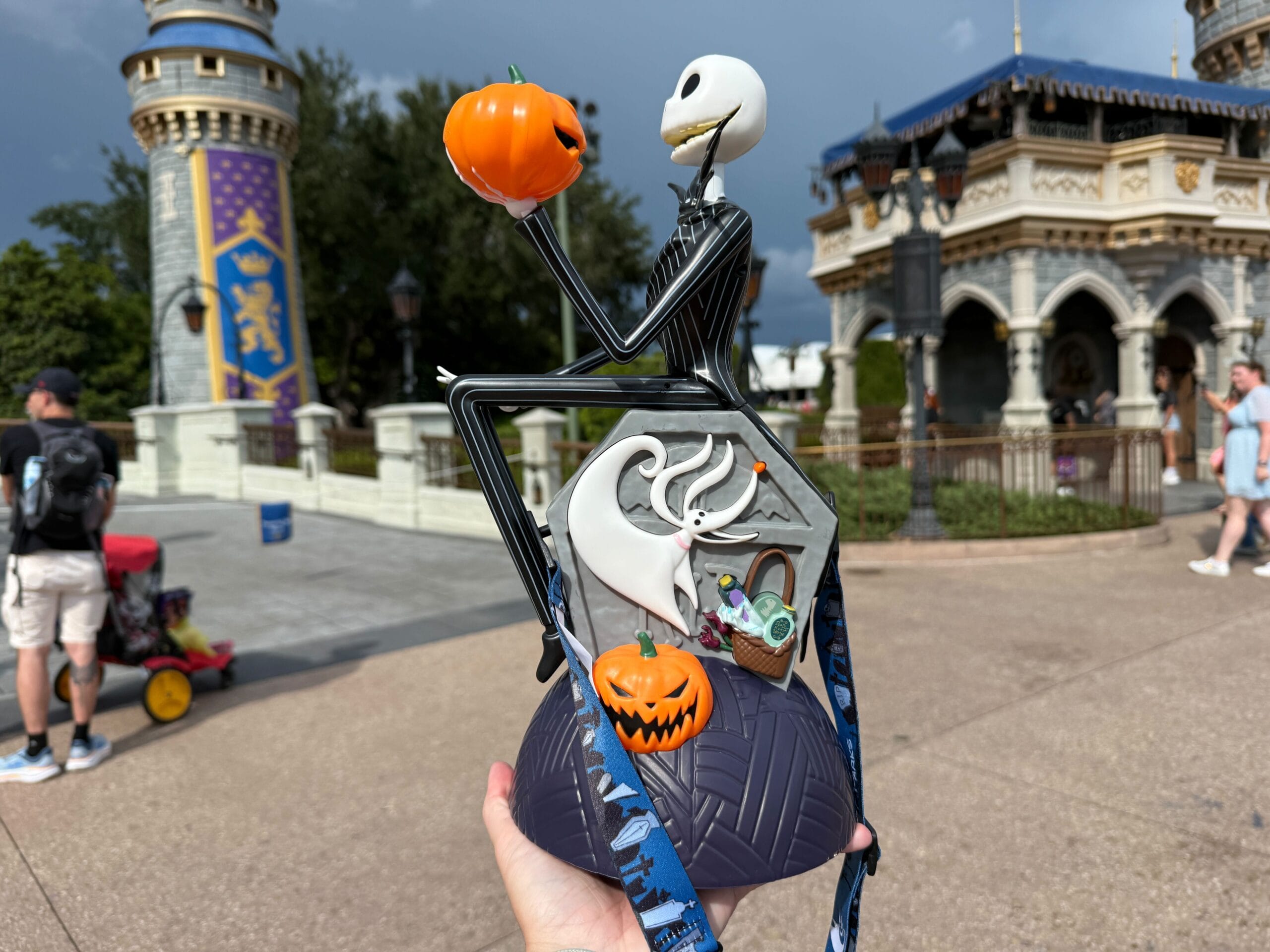 A hand holds a Jack Skellington Popcorn Bucket at Mickey's Not So Scary Halloween Party, with a castle in the background.