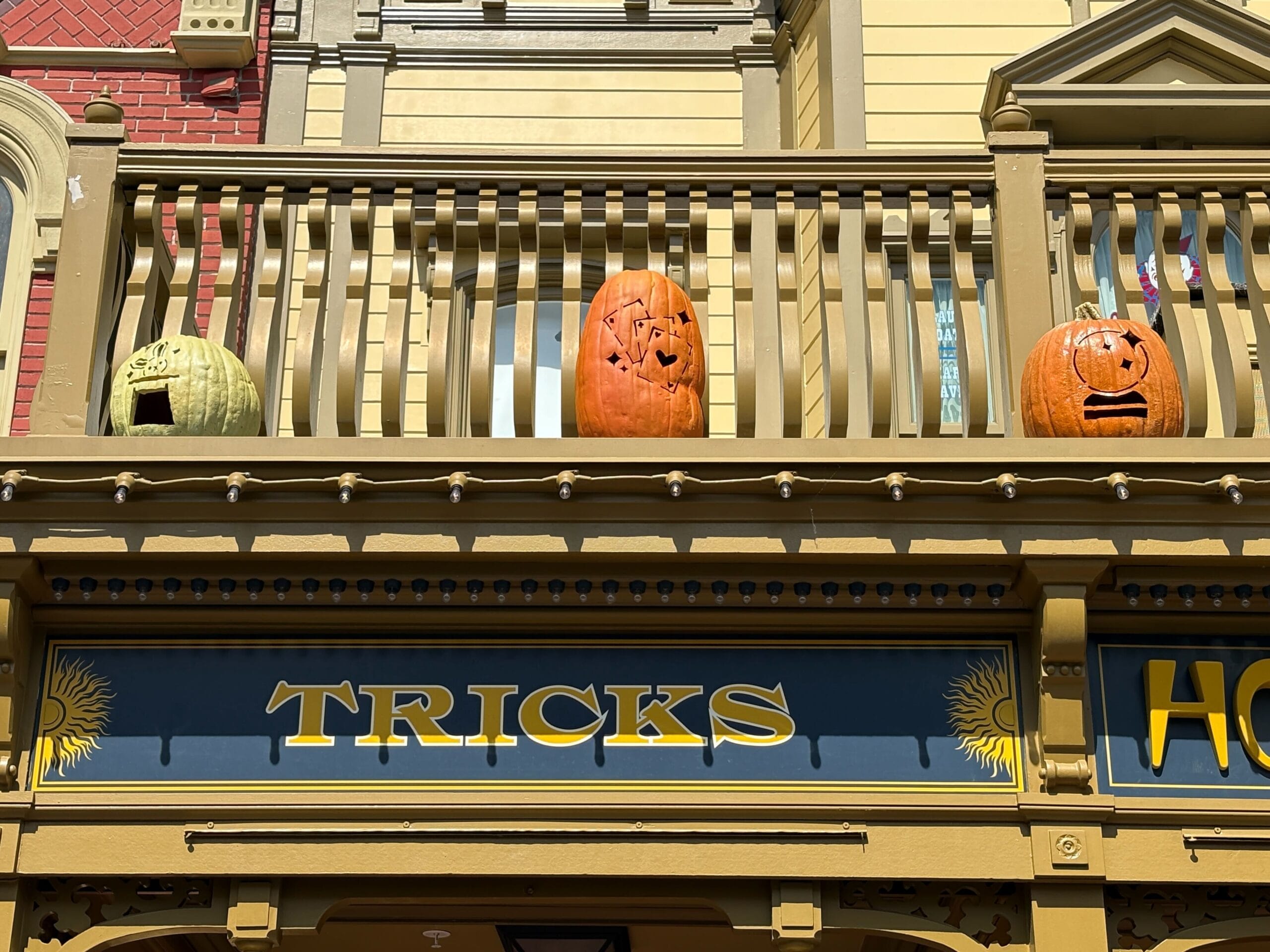 Three carved pumpkins with faces sit on a balcony railing, adding festive Halloween decor above a "TRICKS" sign.