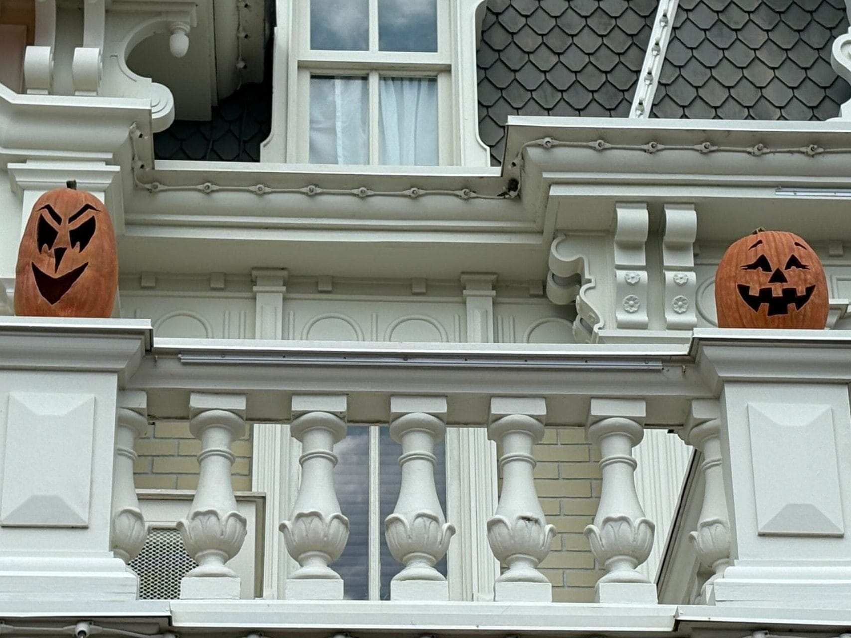 Two carved pumpkin decorations sit on a white balcony with festive Halloween decor and orange and yellow bunting.