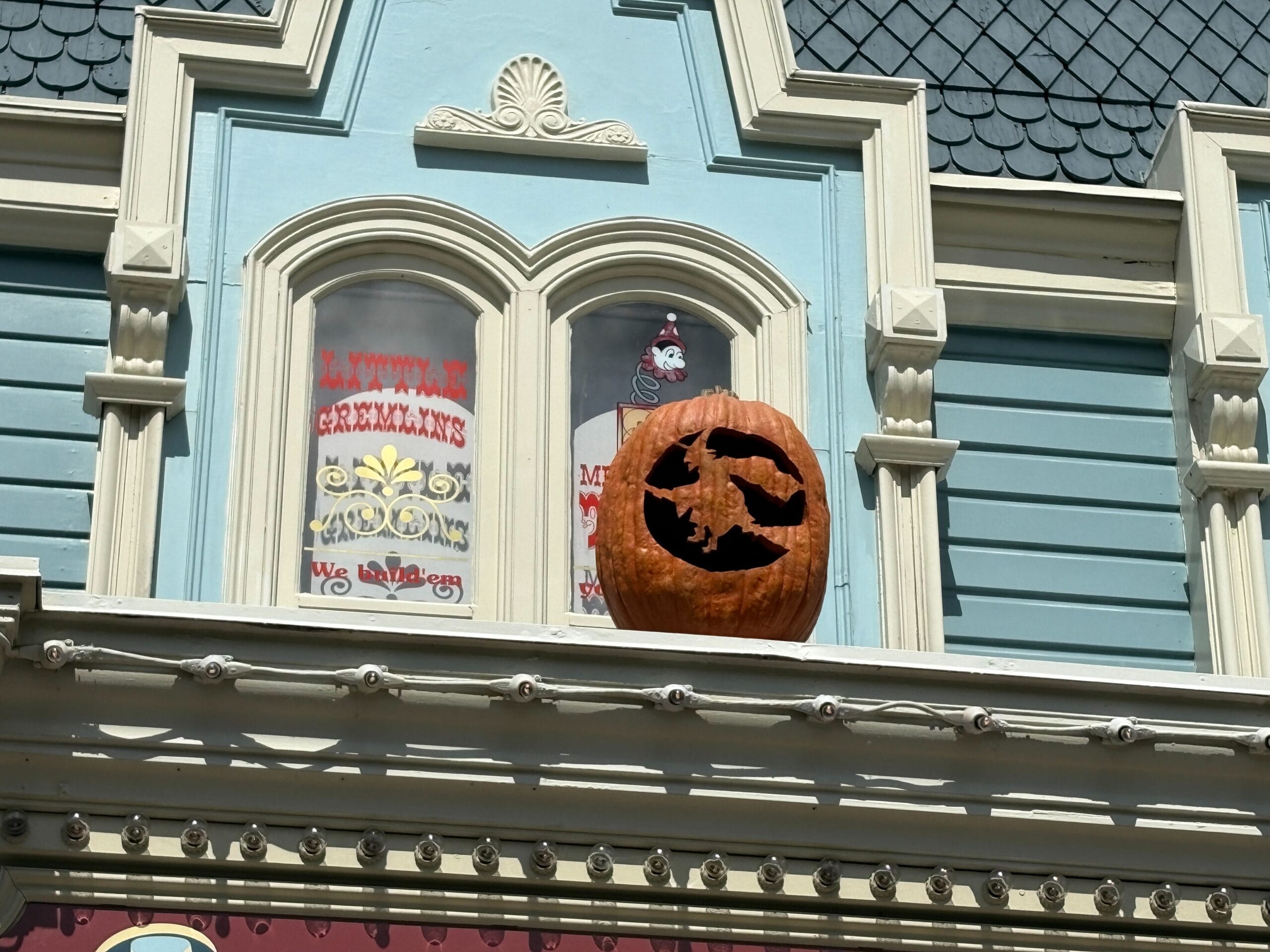 A carved pumpkin featuring a flying witch adds Halloween decor to a building ledge by ornate blue and white windows.