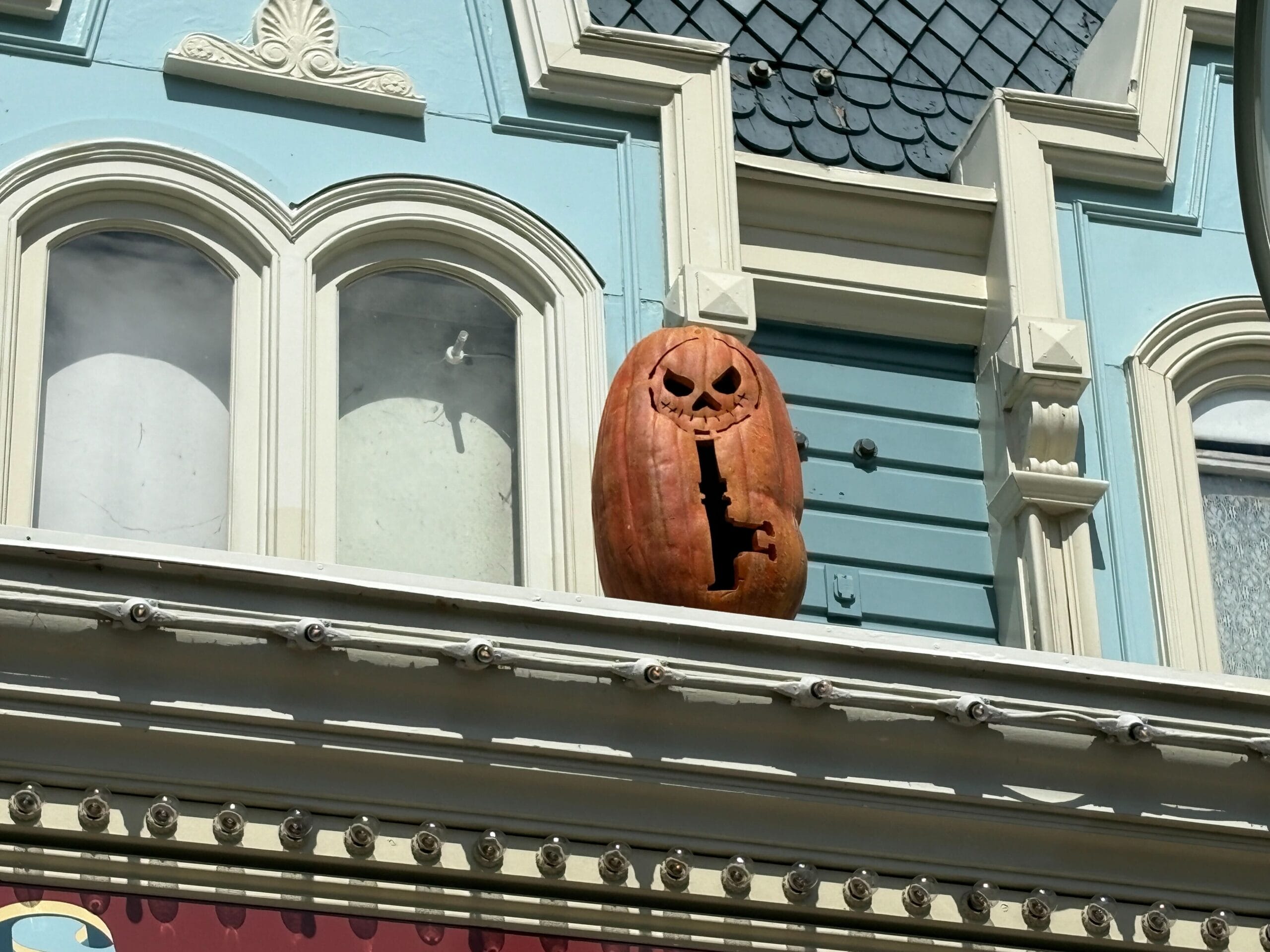 A carved pumpkin with a menacing face sits on a building ledge, adding Halloween decor above arched windows and trim.