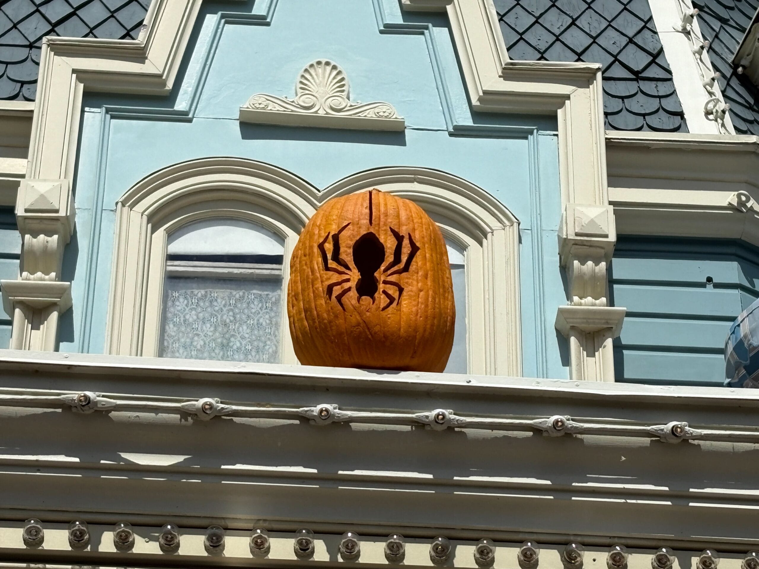 A pumpkin with a spider carving sits on a ledge, adding Halloween Decor to the Magic Kingdom's blue and white facade.