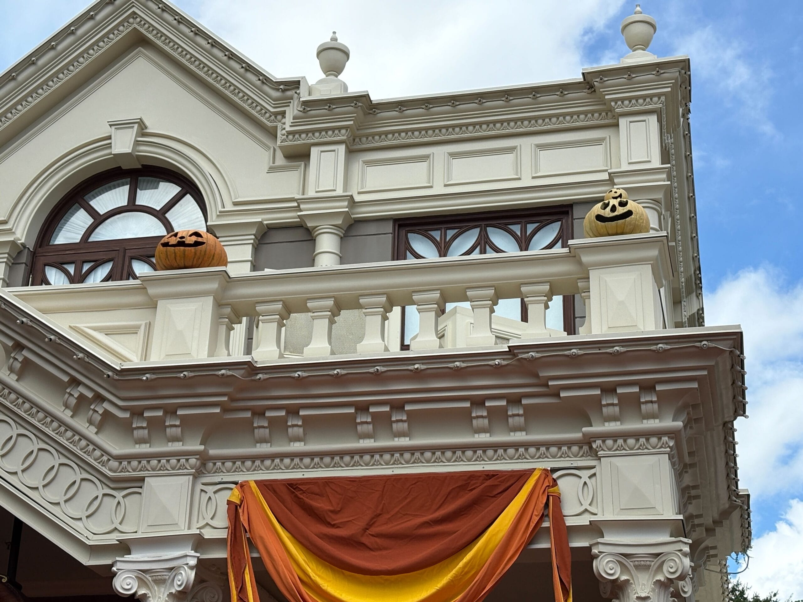White building with Halloween decor—carved pumpkins and orange-yellow fabric—evoking Magic Kingdom charm under a blue sky.
