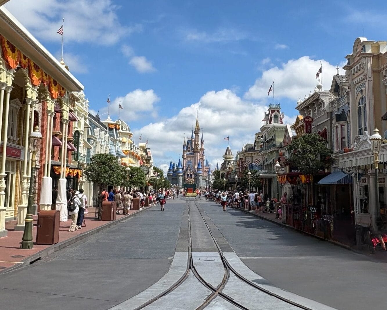 Main Street, U.S.A. in Magic Kingdom features Halloween Decor with Cinderella Castle under a blue, cloud-scattered sky.