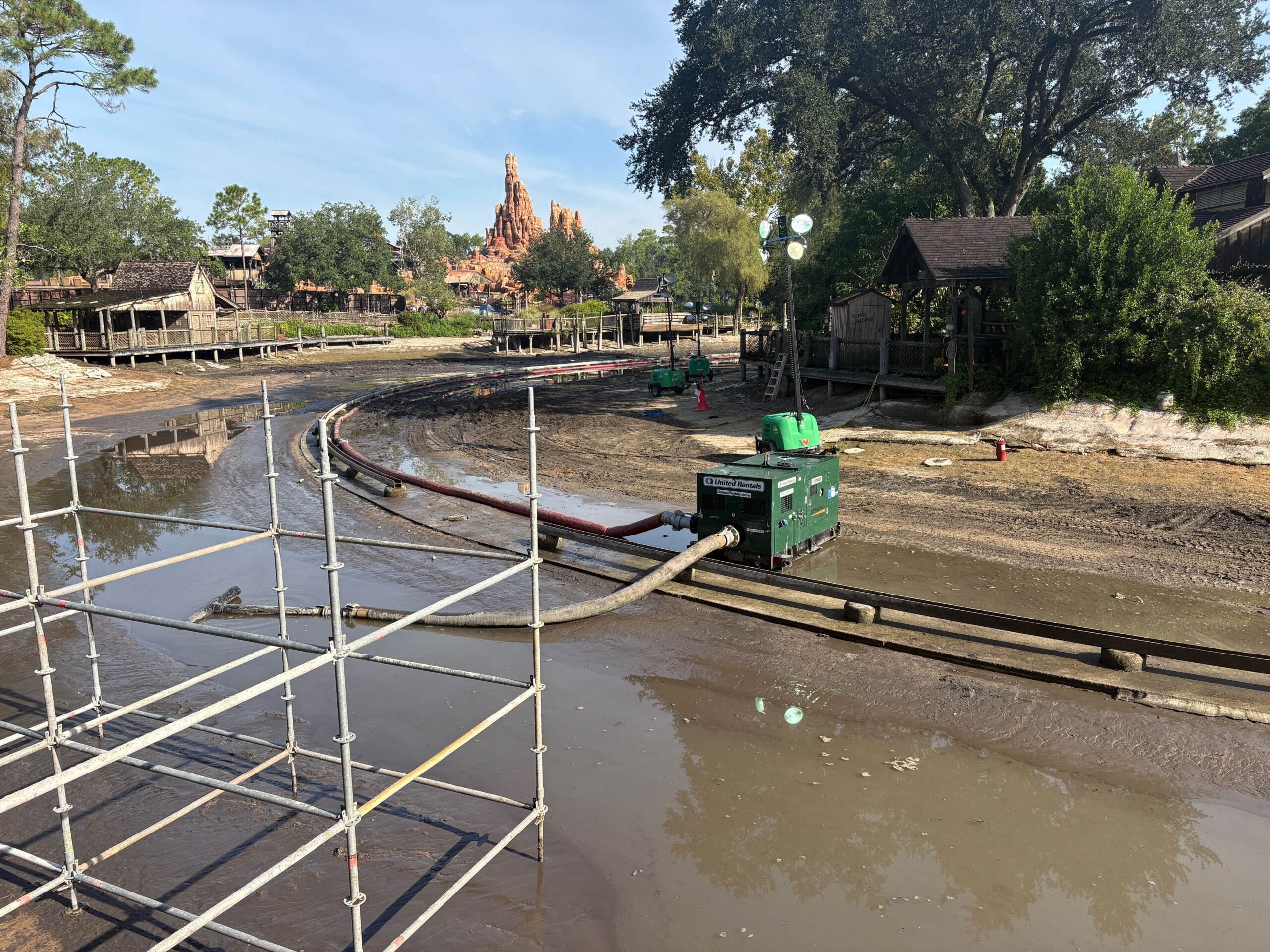 A drained theme park water ride under maintenance, with exposed tracks, scaffolding, and a pump in view.