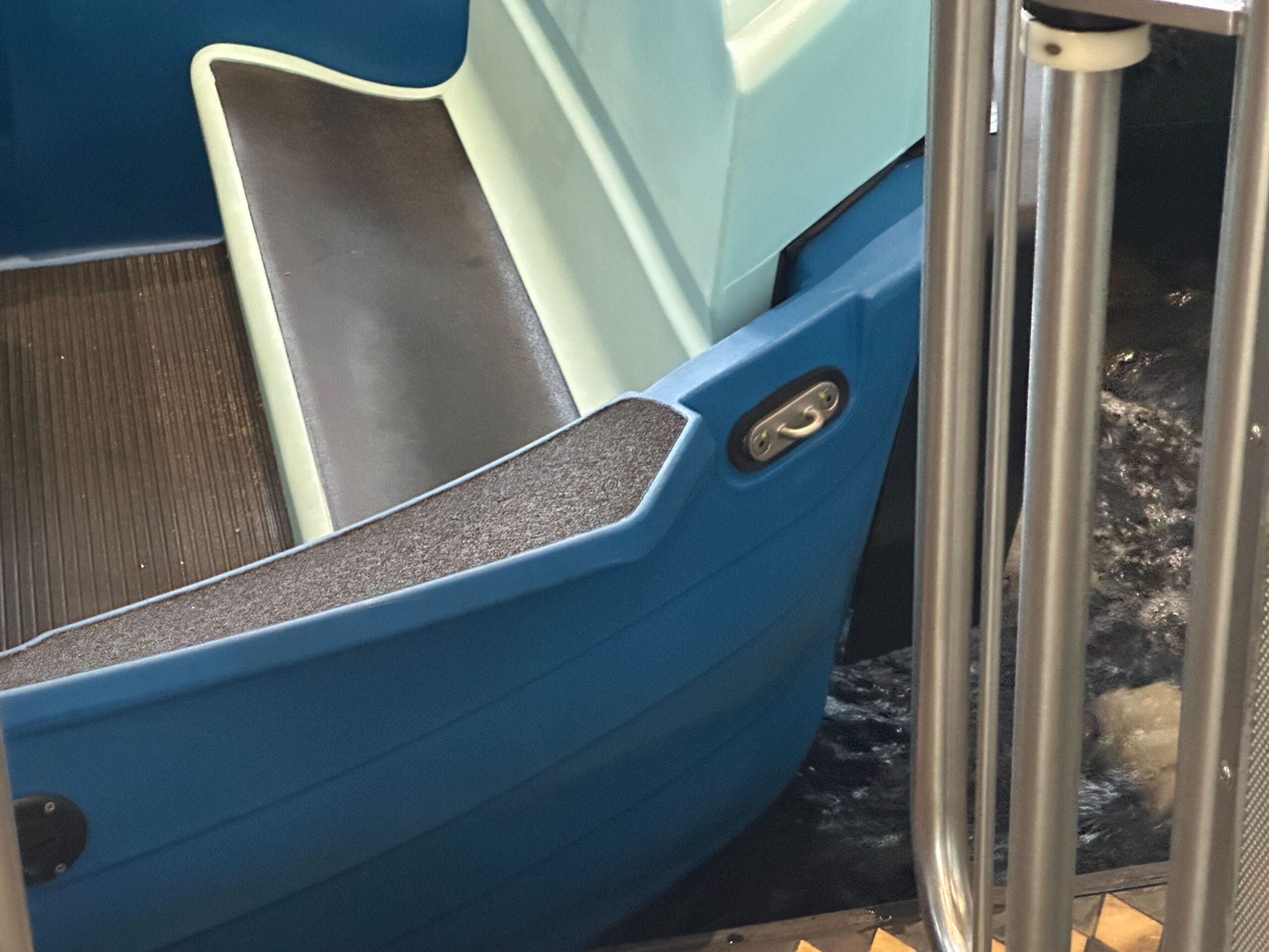 Close-up of a blue ride boat from "it's a small world" at Magic Kingdom, beside a metal railing and water below.