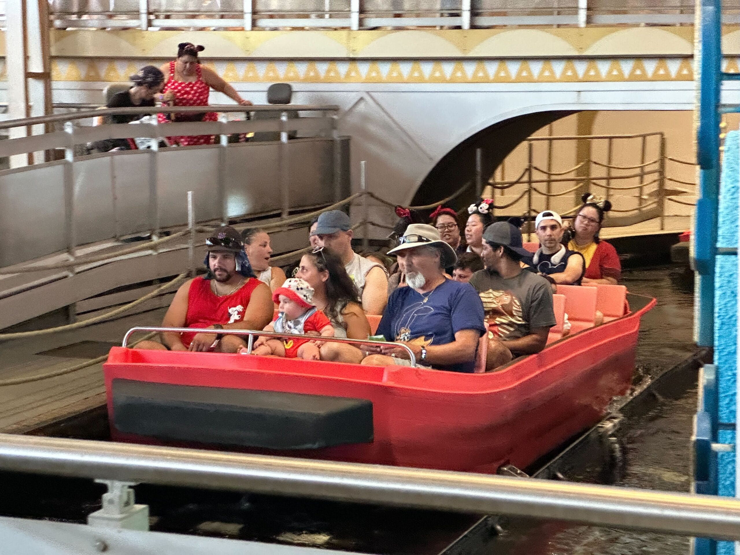 A group in Mickey ears ride new boats inside Magic Kingdom’s “it’s a small world,” looking ahead with excitement.