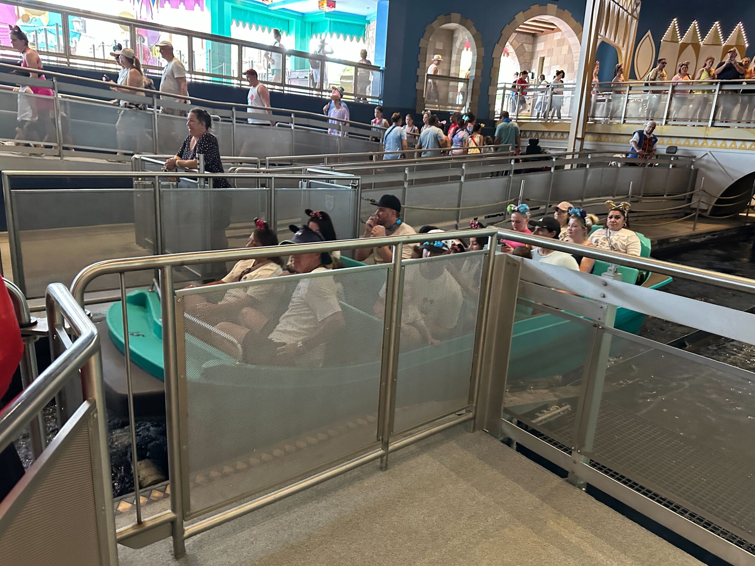 Guests sit in new boats at the "it’s a small world" ride at Magic Kingdom, while others wait behind metal railings.