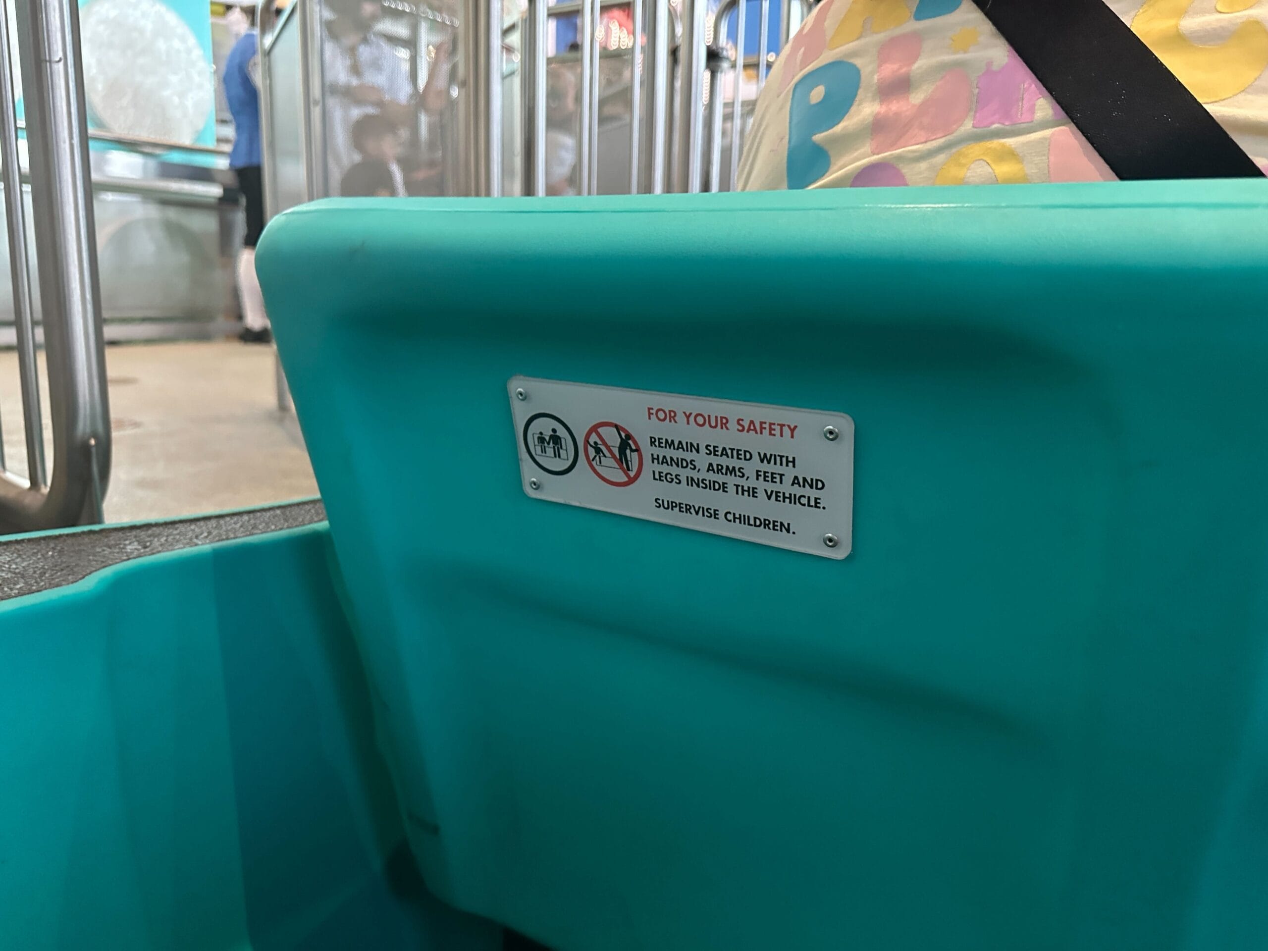A teal ride seat on the Magic Kingdom "it’s a small world" boats with a sign to remain seated and supervise children.