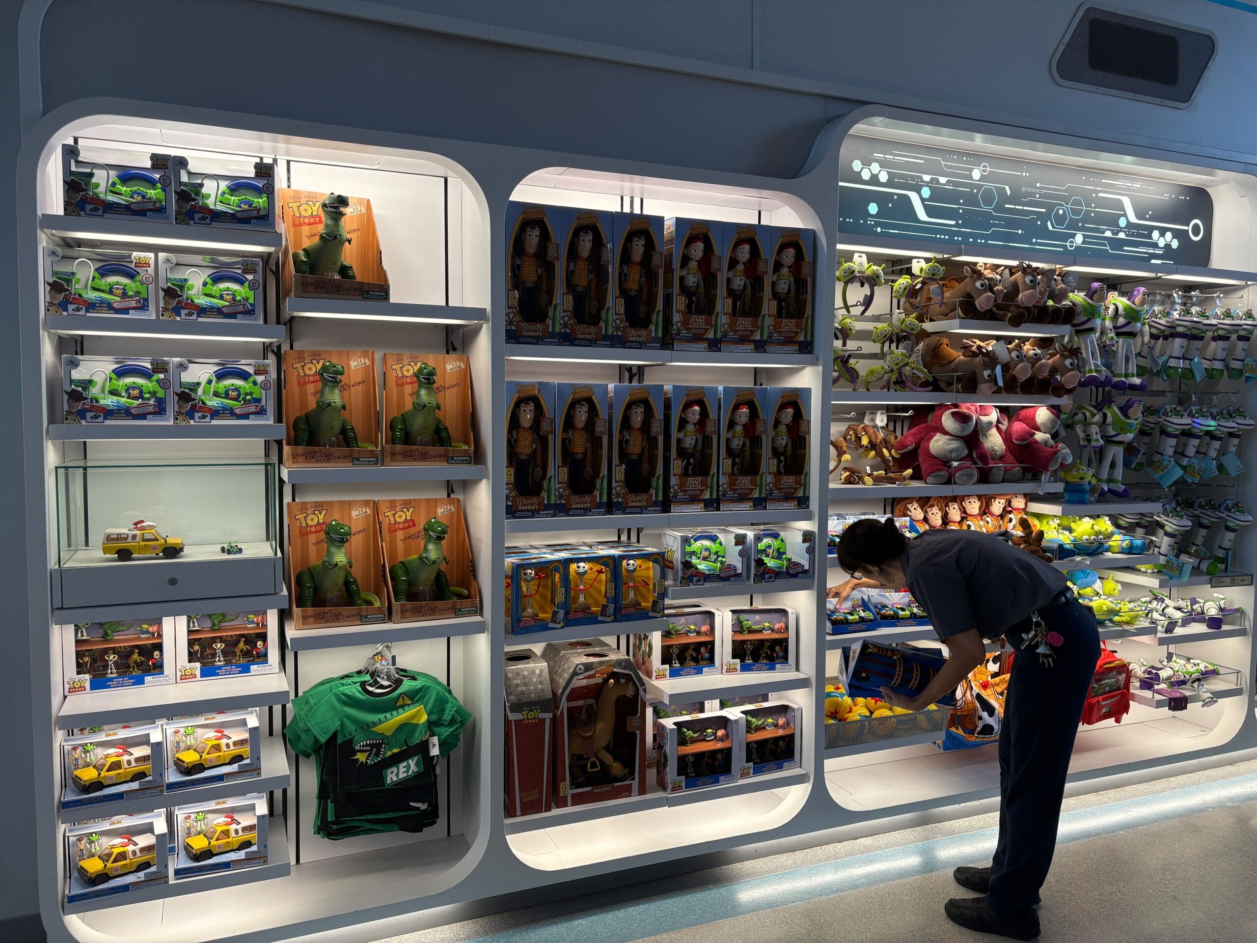 A person arranges Toy Story merchandise on brightly lit shelves in a retail store.