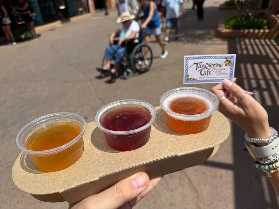 Three small cups of New Food & Wine on a cardboard holder; Tangerine Café card held outdoors in the background.