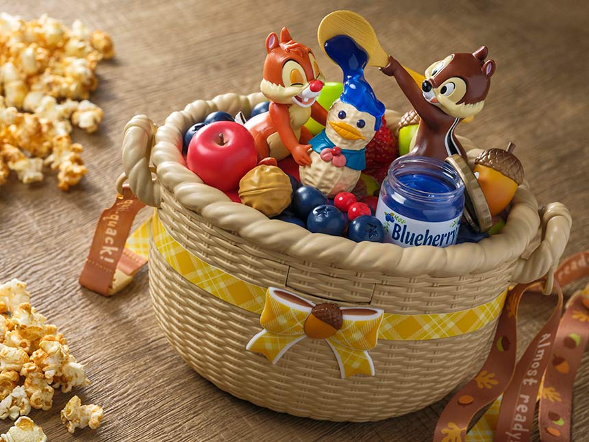 A Harvest Bucket picnic basket with Chip 'n' Dale figurines, fruit, blueberry jam, and scattered popcorn nearby.