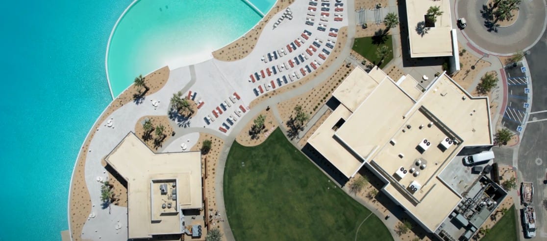 Aerial view of Disney Cotino Community buildings, parked cars, green lawn, and a large blue pool with a sandy edge.
