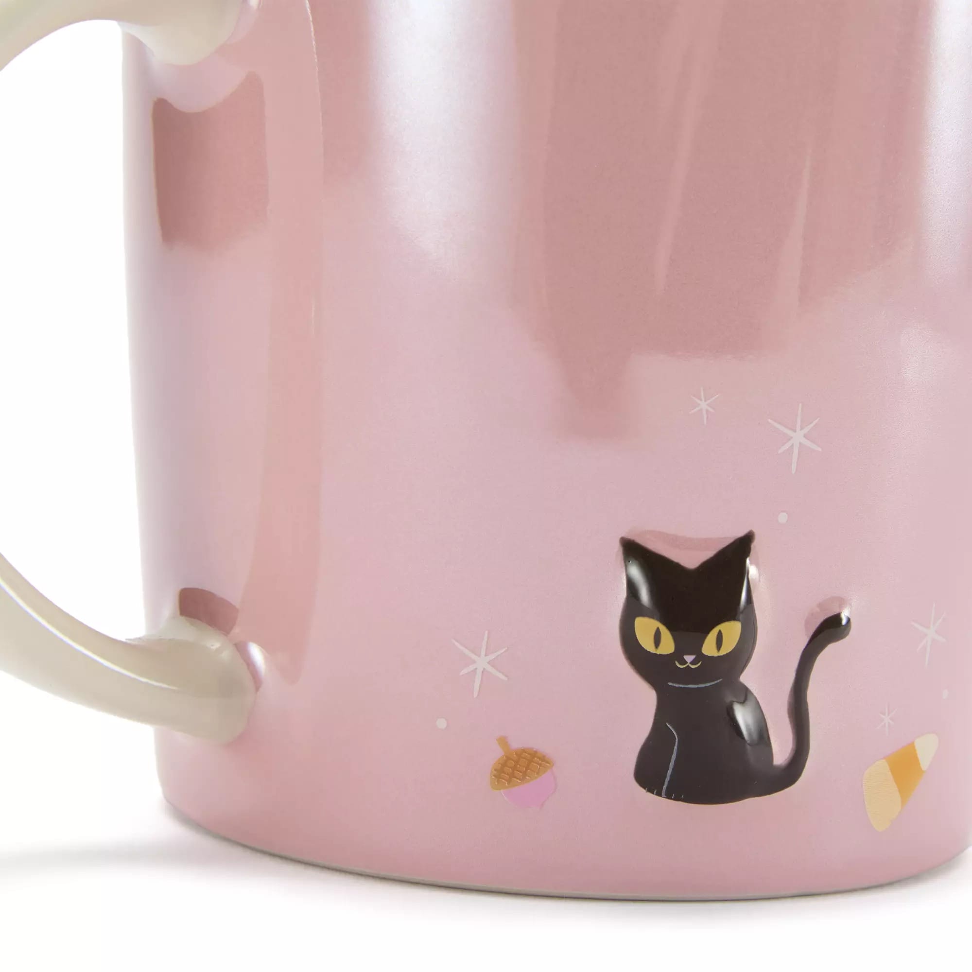 A pink mug with a drawing of a black cat, an acorn, and a piece of candy corn near the handle.