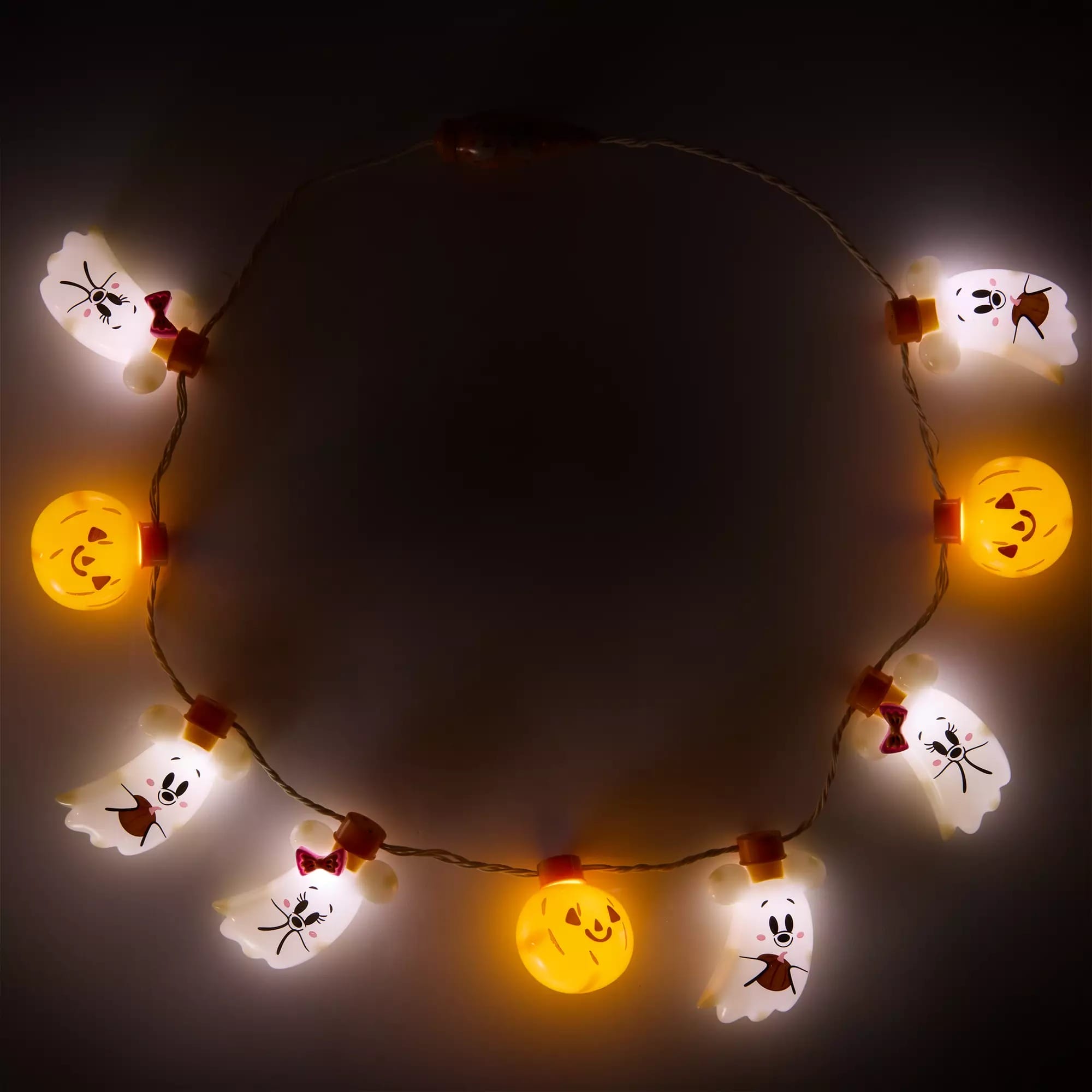 A string of glowing Halloween lights shaped like ghosts and jack-o’-lanterns arranged in a circle in the dark.