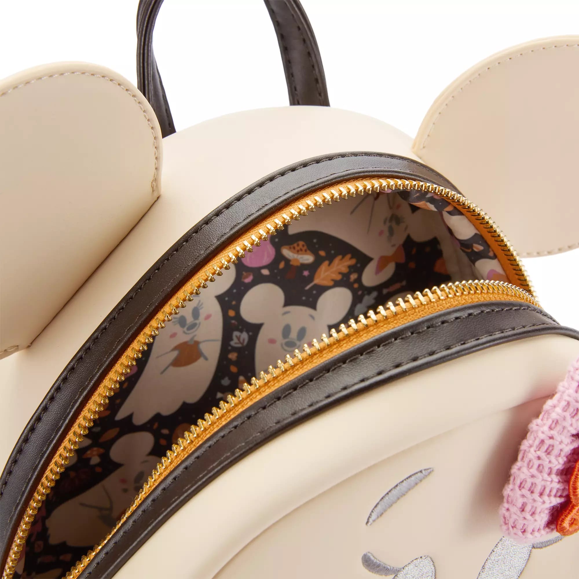 Close-up of a cream-colored backpack with ear shapes and opened zipper, revealing a patterned fabric lining inside.