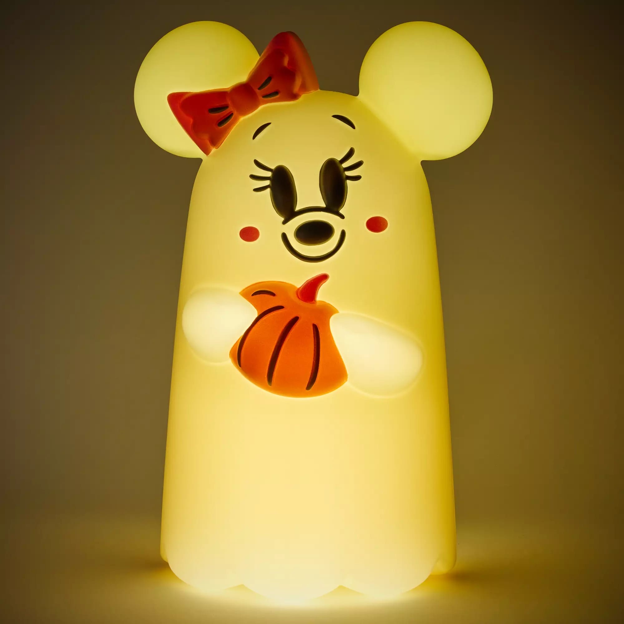A cute ghost-shaped night light with mouse ears, a red bow, and holding an orange pumpkin.