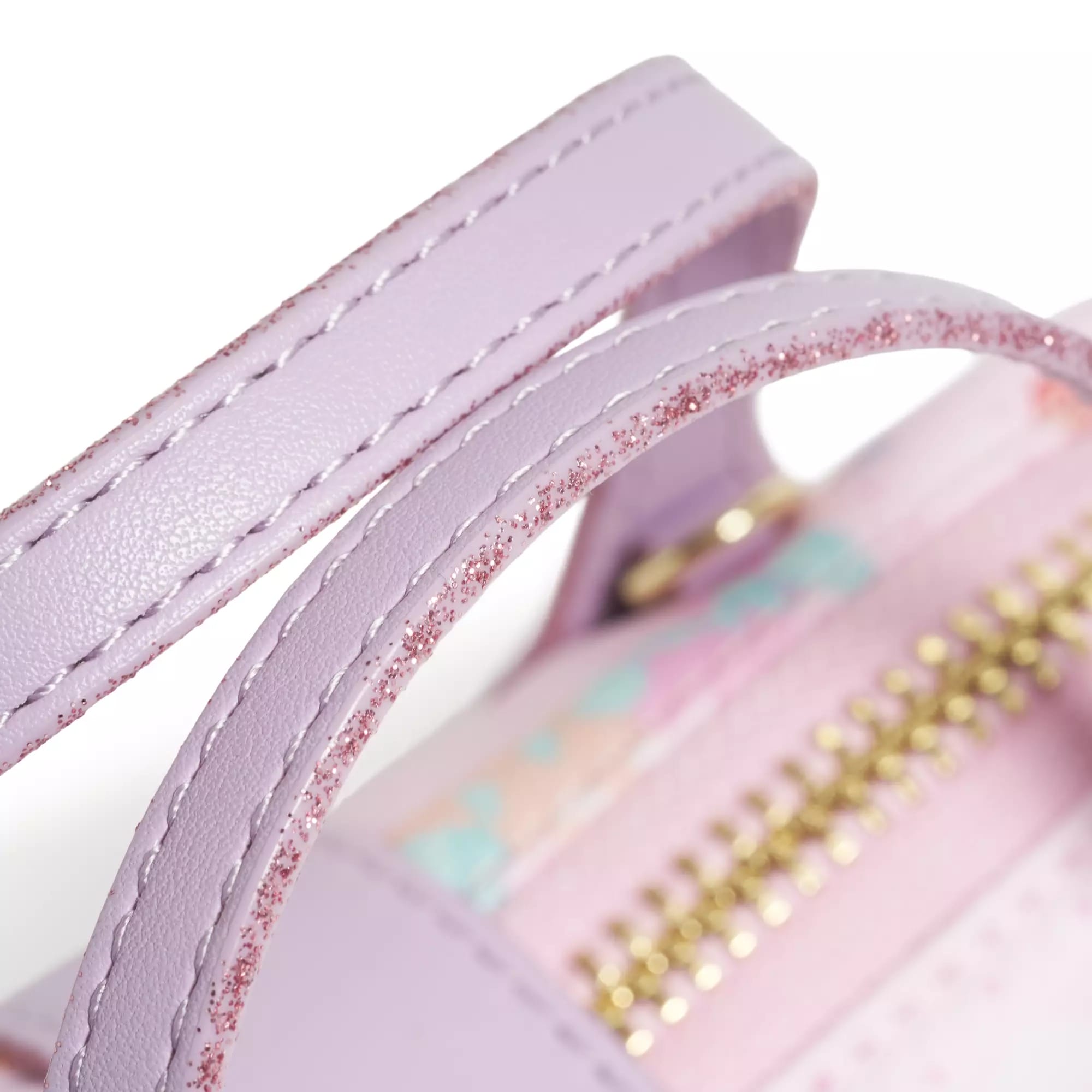 Close-up of a pastel purple bag handle with pink glitter and a gold zipper on a light pink background.