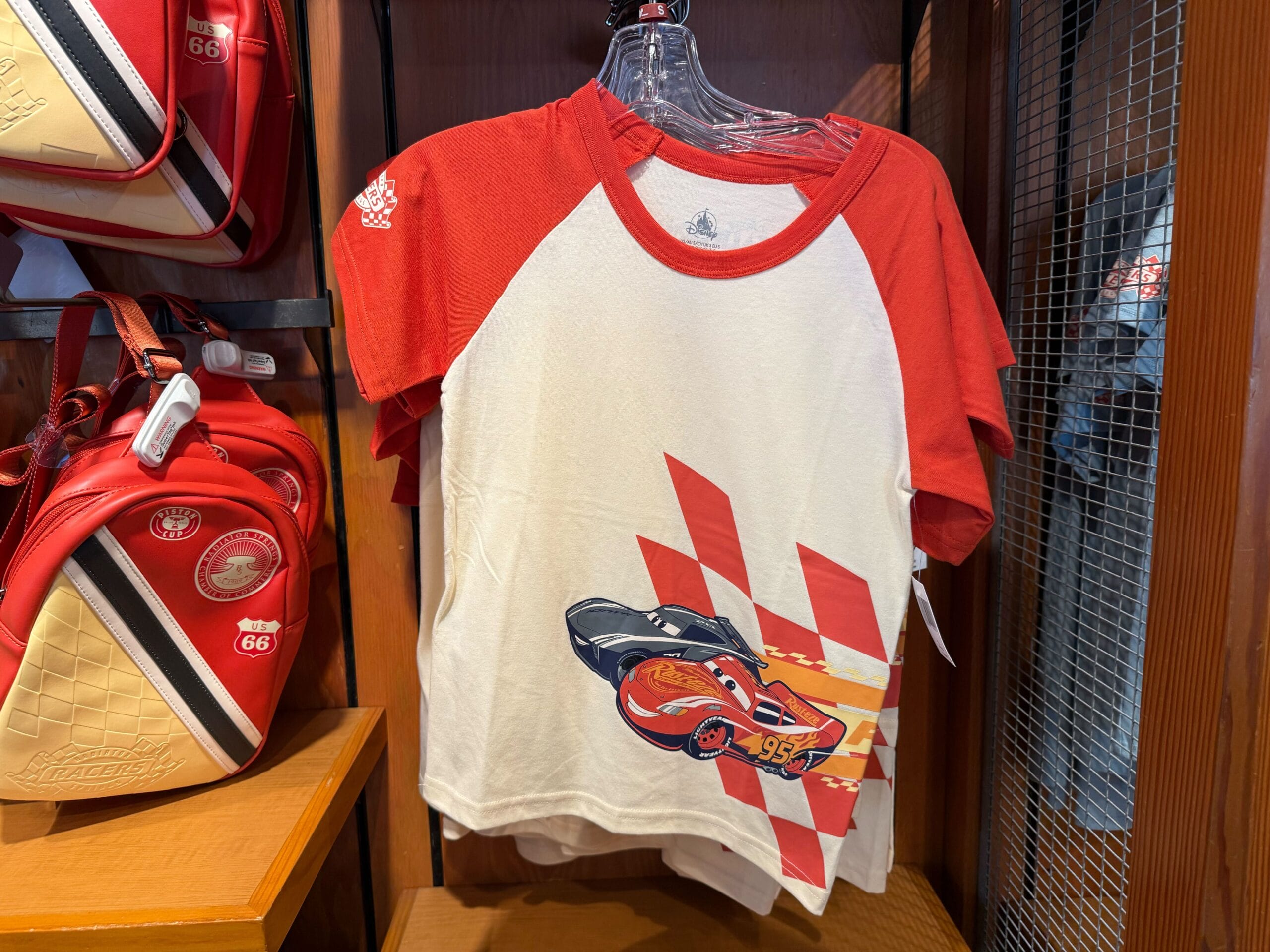 Red and white T-shirt with a Cars character and checkered flag design displayed in a store.