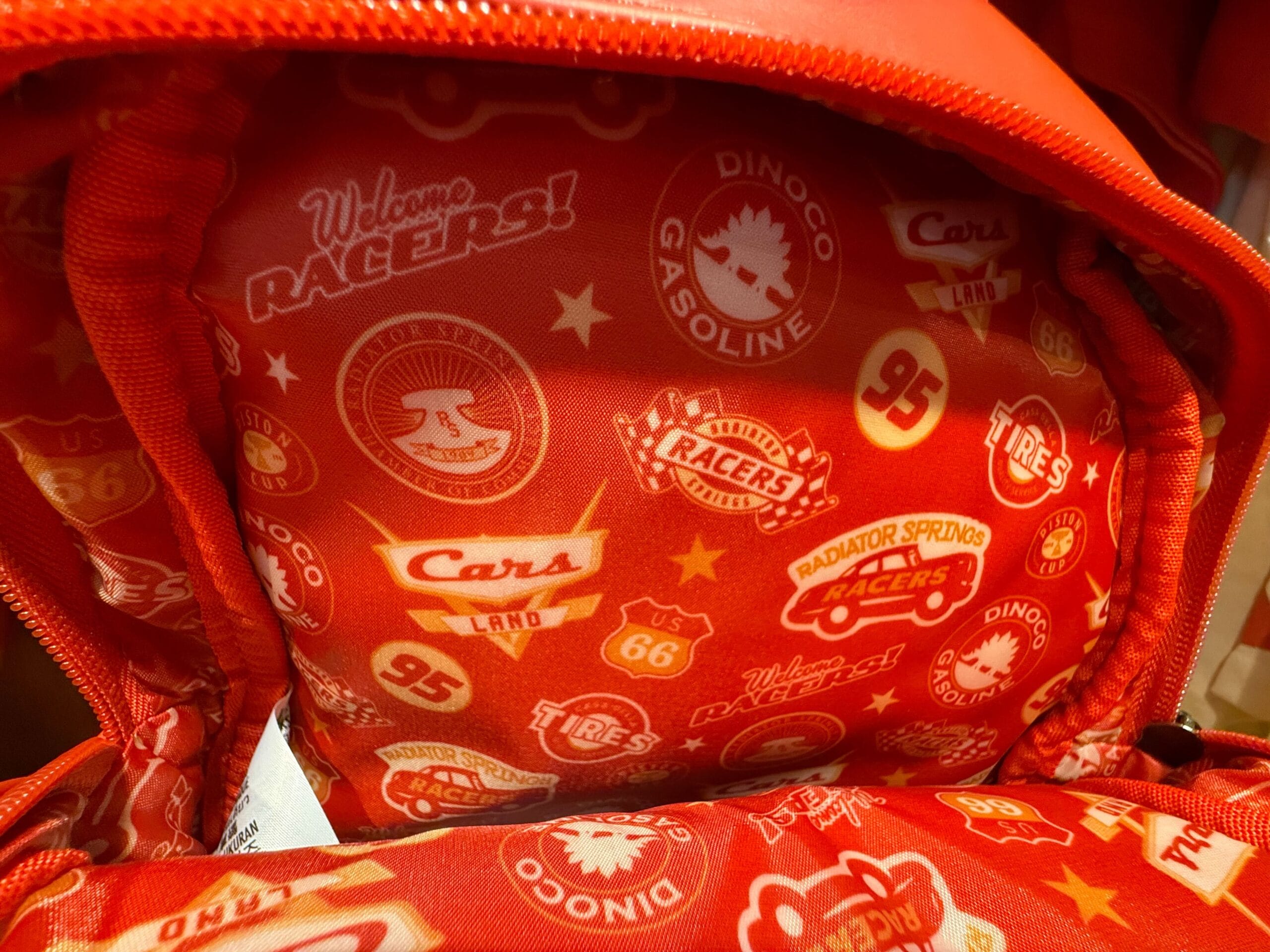 Red backpack interior with various Cars movie-themed logos, including Lightning McQueen's number 95 and Radiator Springs.
