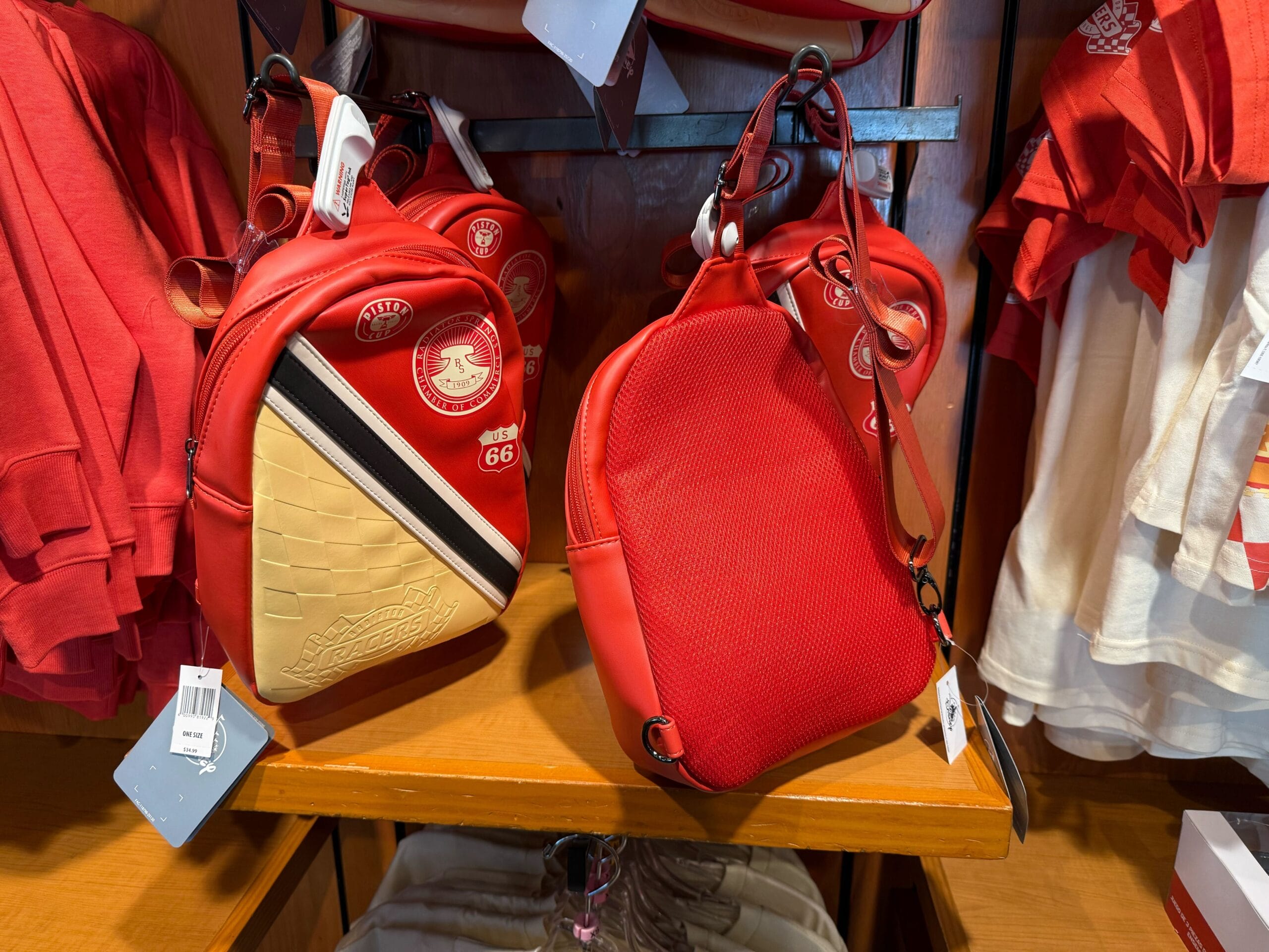 Two red mini backpacks with badges on display shelf, one showing tan front panel, surrounded by red clothing.