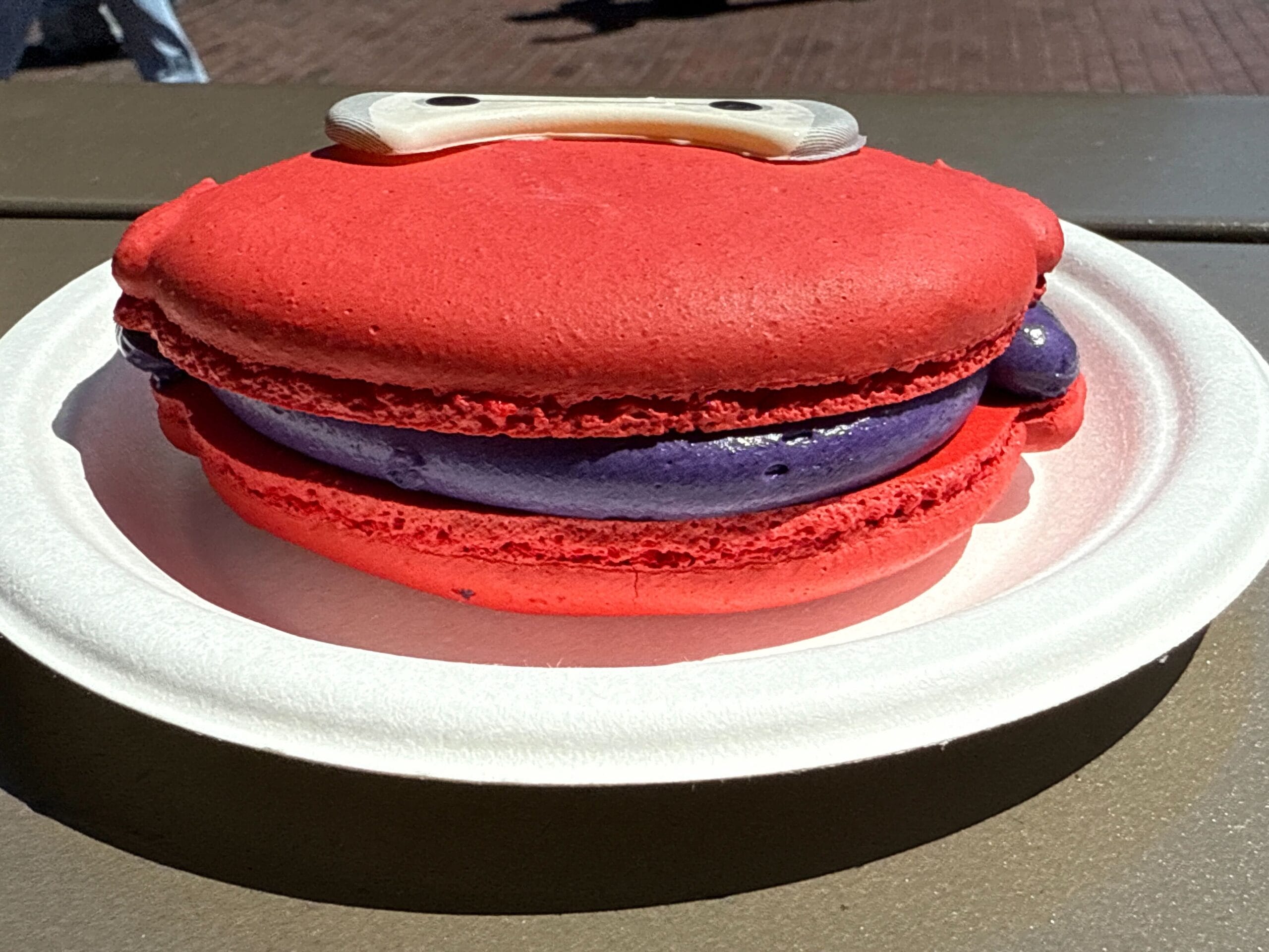 An Ube Baymax Macaron with purple filling and cartoon eyes, served outdoors at Disney California Adventure.