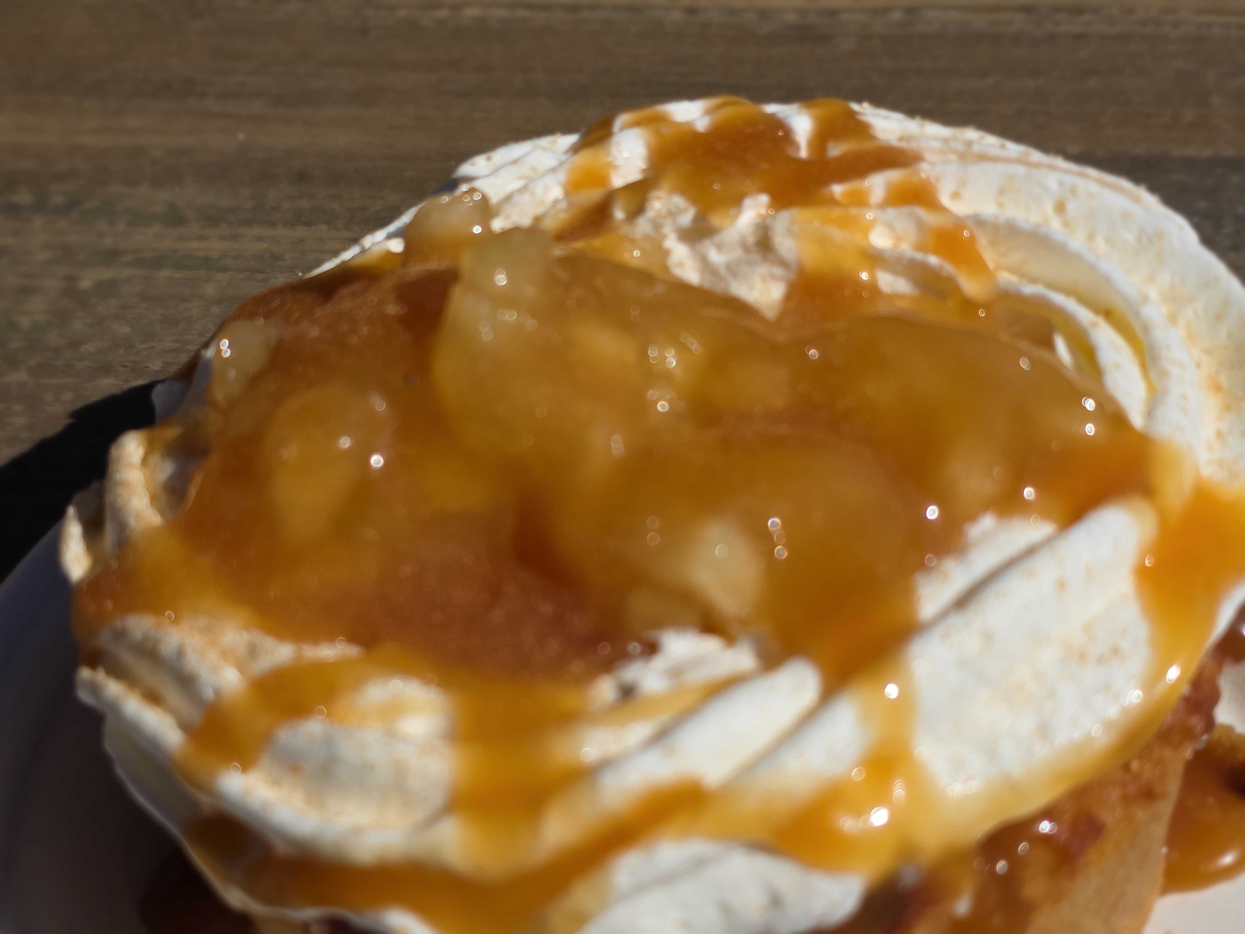 A dessert from Aunt Cass Cafe topped with whipped cream and caramel sauce sits on a wooden surface.