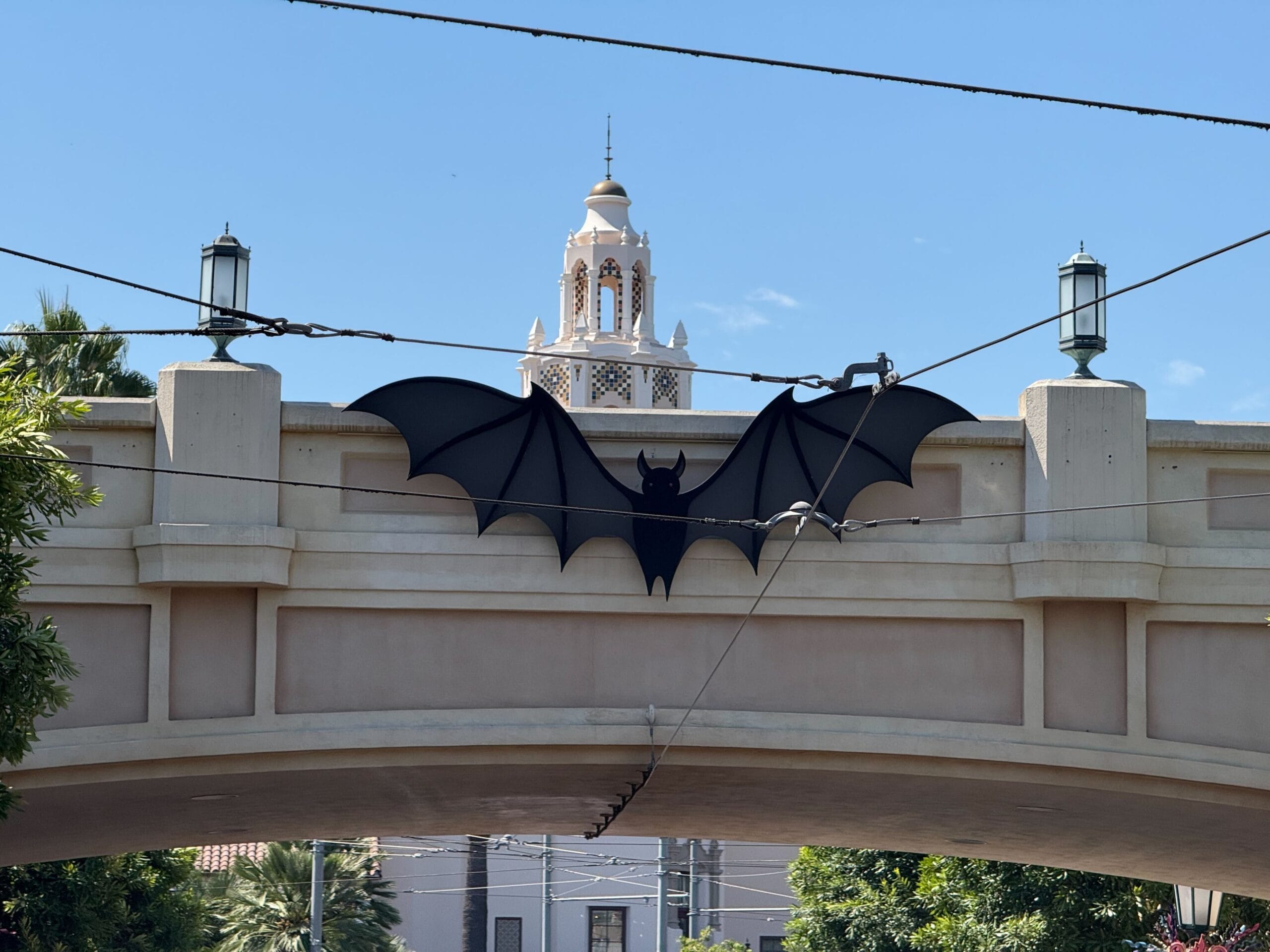 Large black bat decoration on a Buena Vista Street bridge with Carthay Circle Restaurant and blue sky in the background.