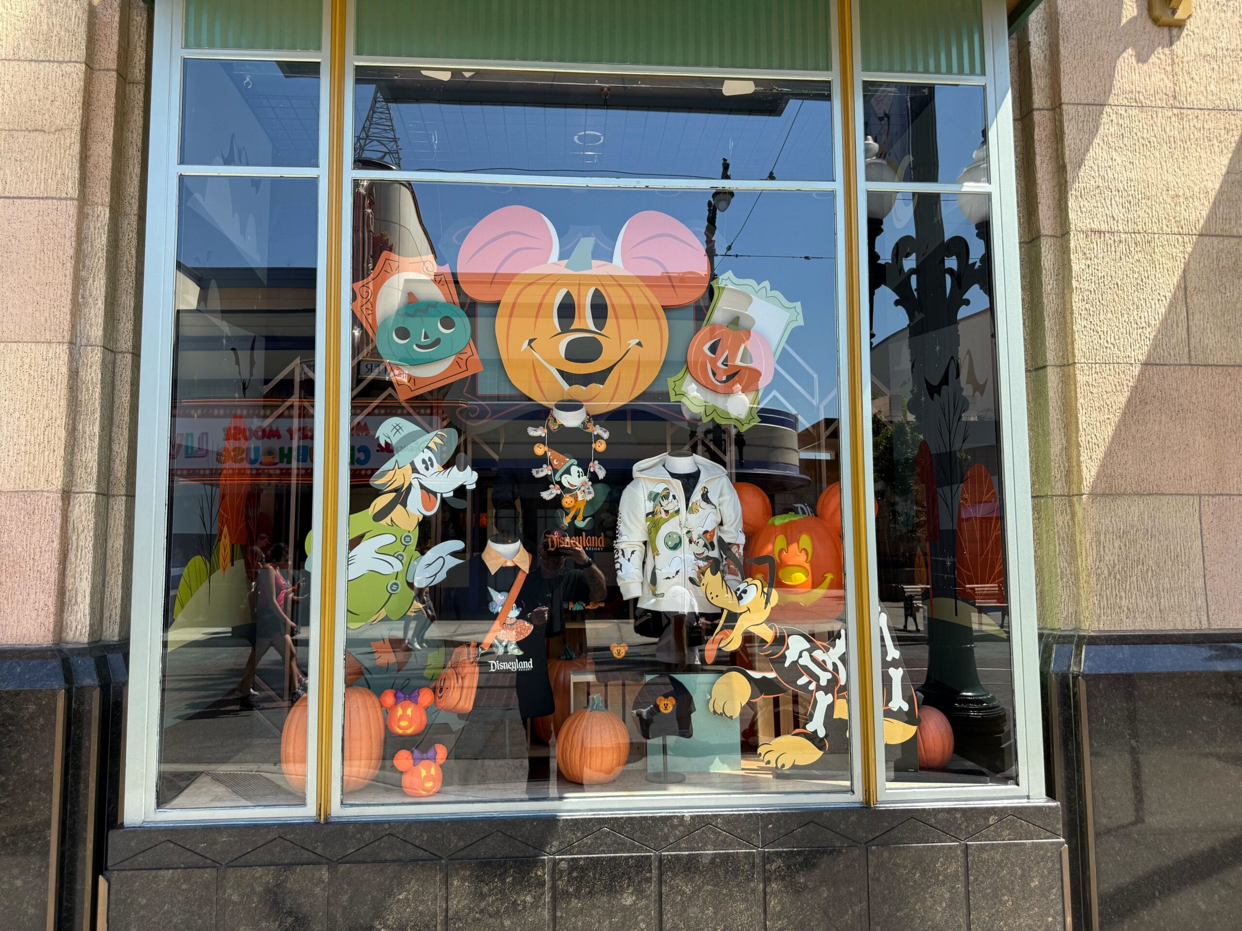 Store window decorated with Disney Halloween characters, pumpkins, and themed merchandise on display.