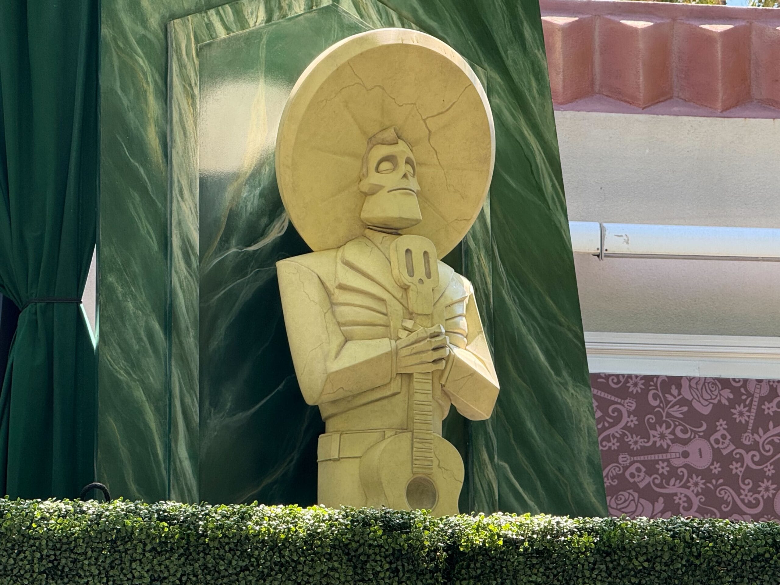 A statue of Ernesto de la Cruz holding a guitar stands in front of green curtains and patterned walls.
