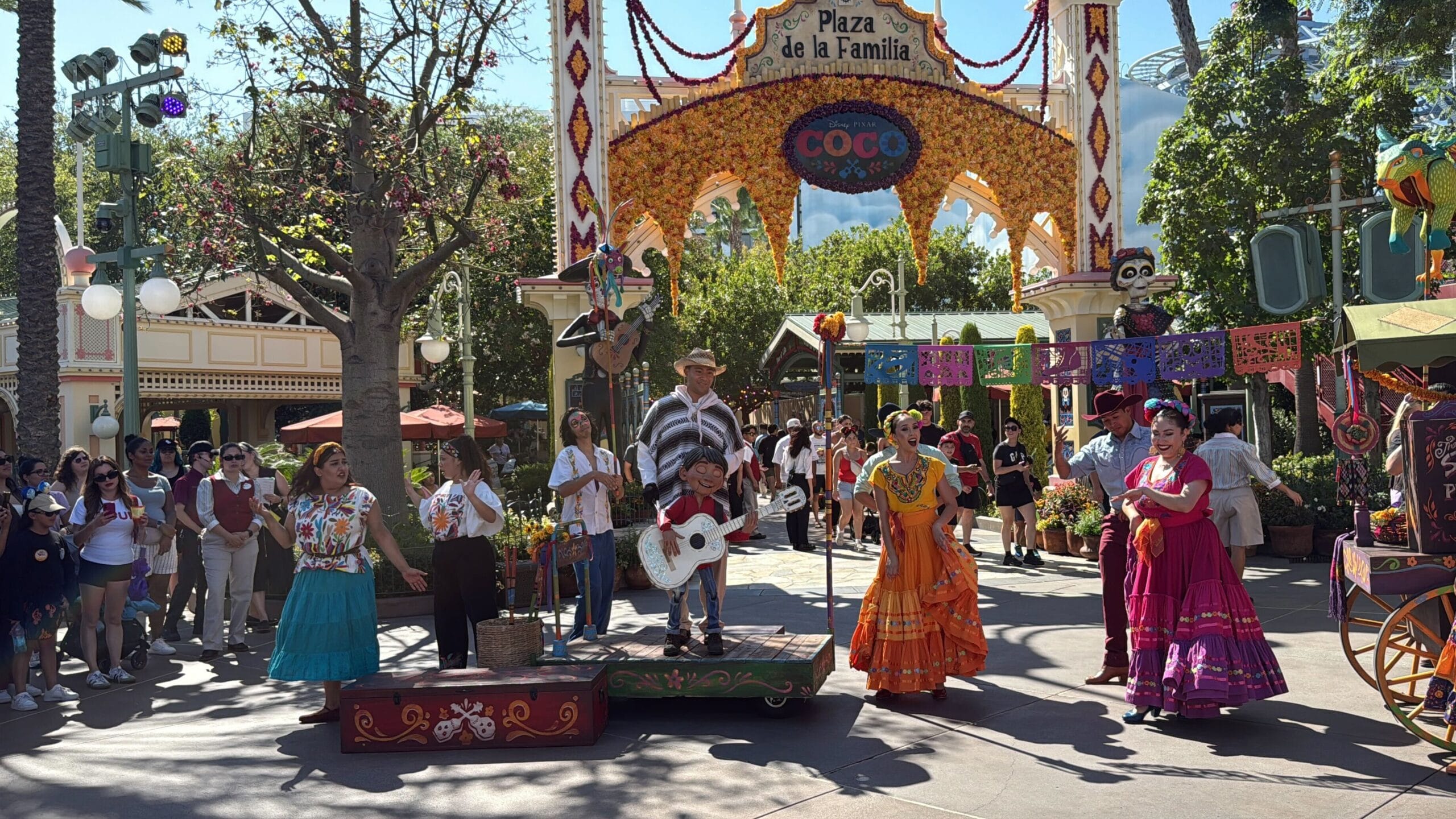 A festive Coco-themed show with vibrant dancers at Plaza de la Familia in Disney California Adventure, daytime.
