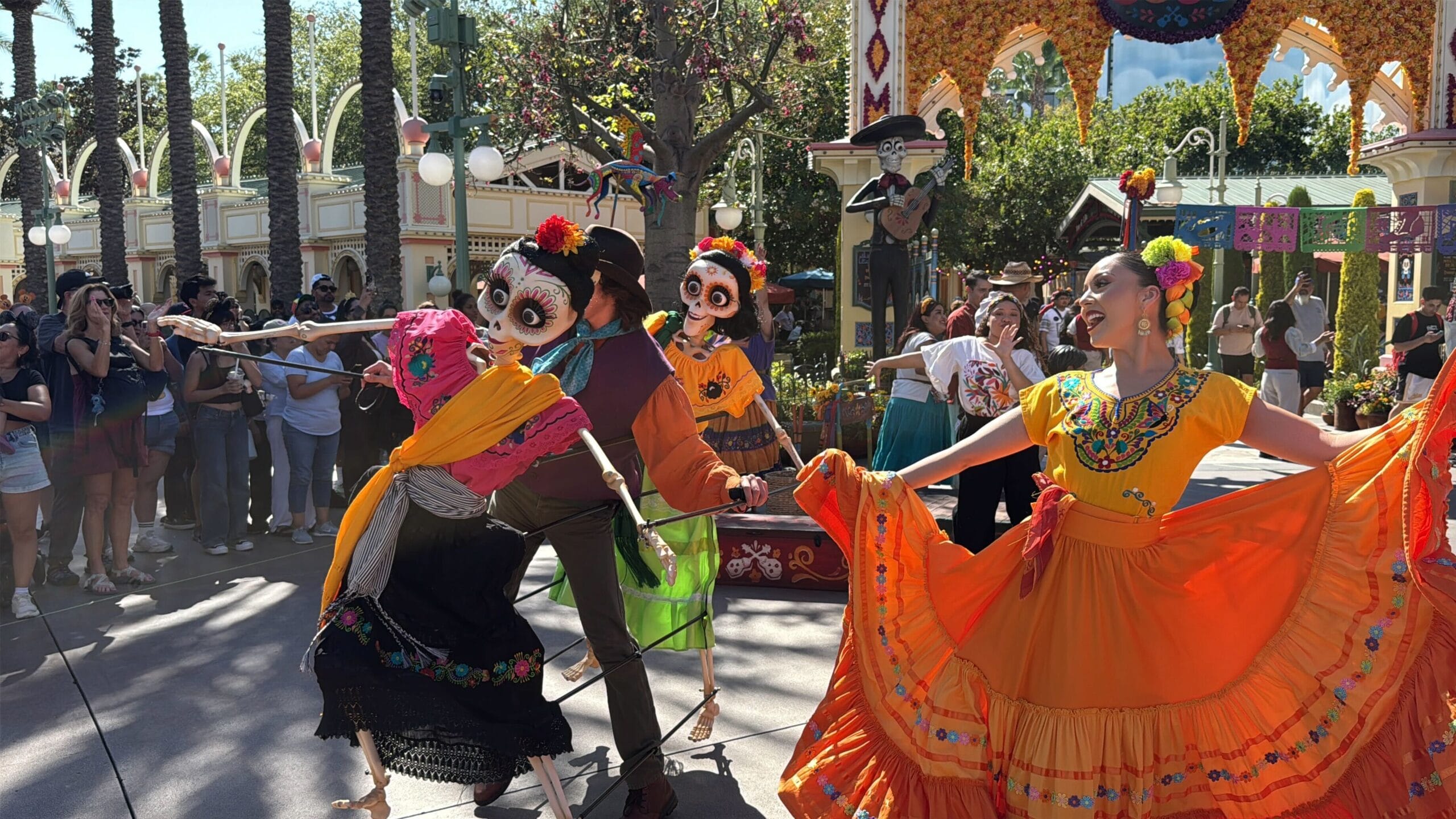Performers in colorful costumes and painted faces dance at Plaza de la Familia in Disney California Adventure.