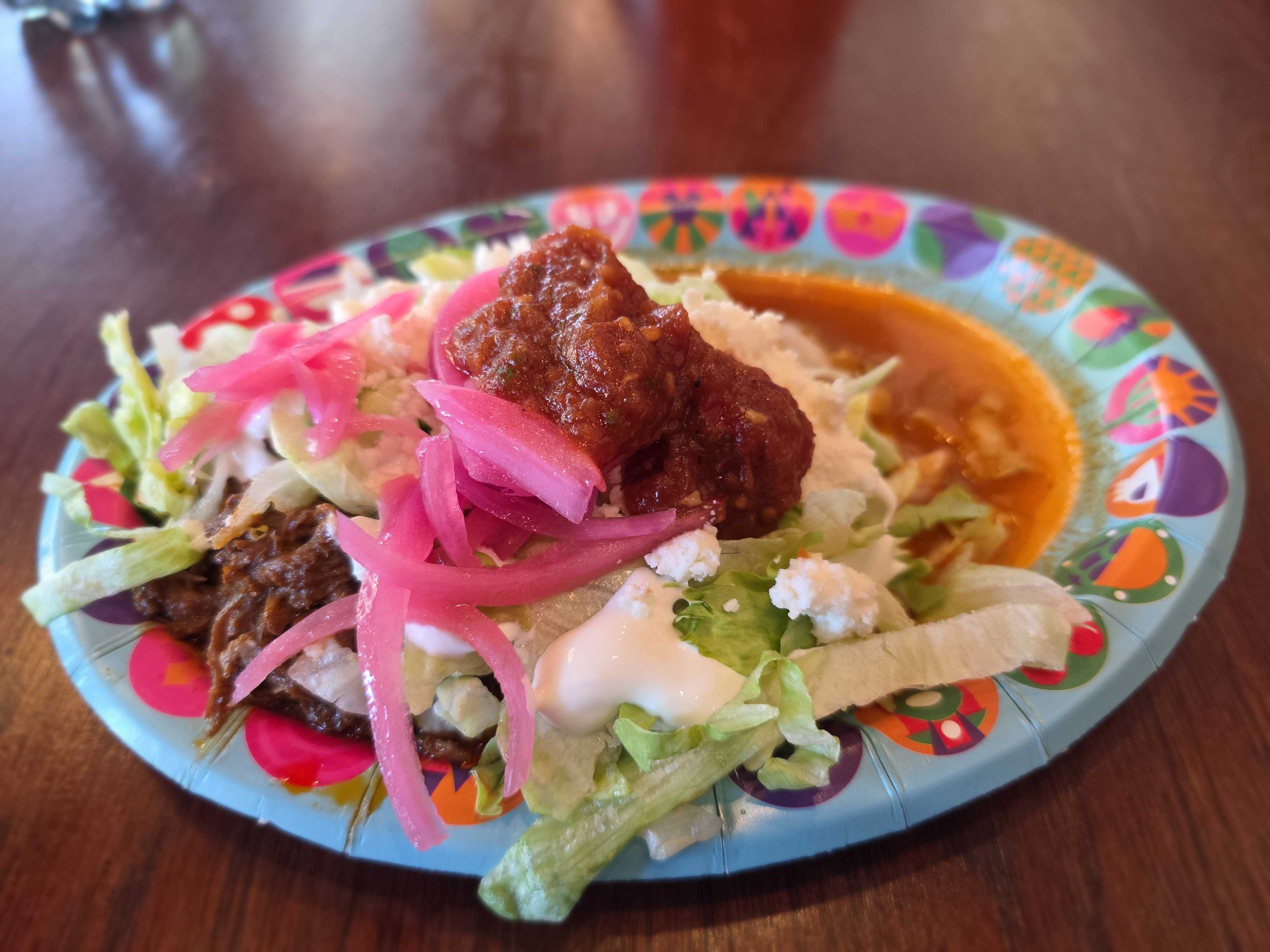 A colorful plate at Cozy Cone Motel features a tostada topped with lettuce, pickled onions, cheese, and salsa.
