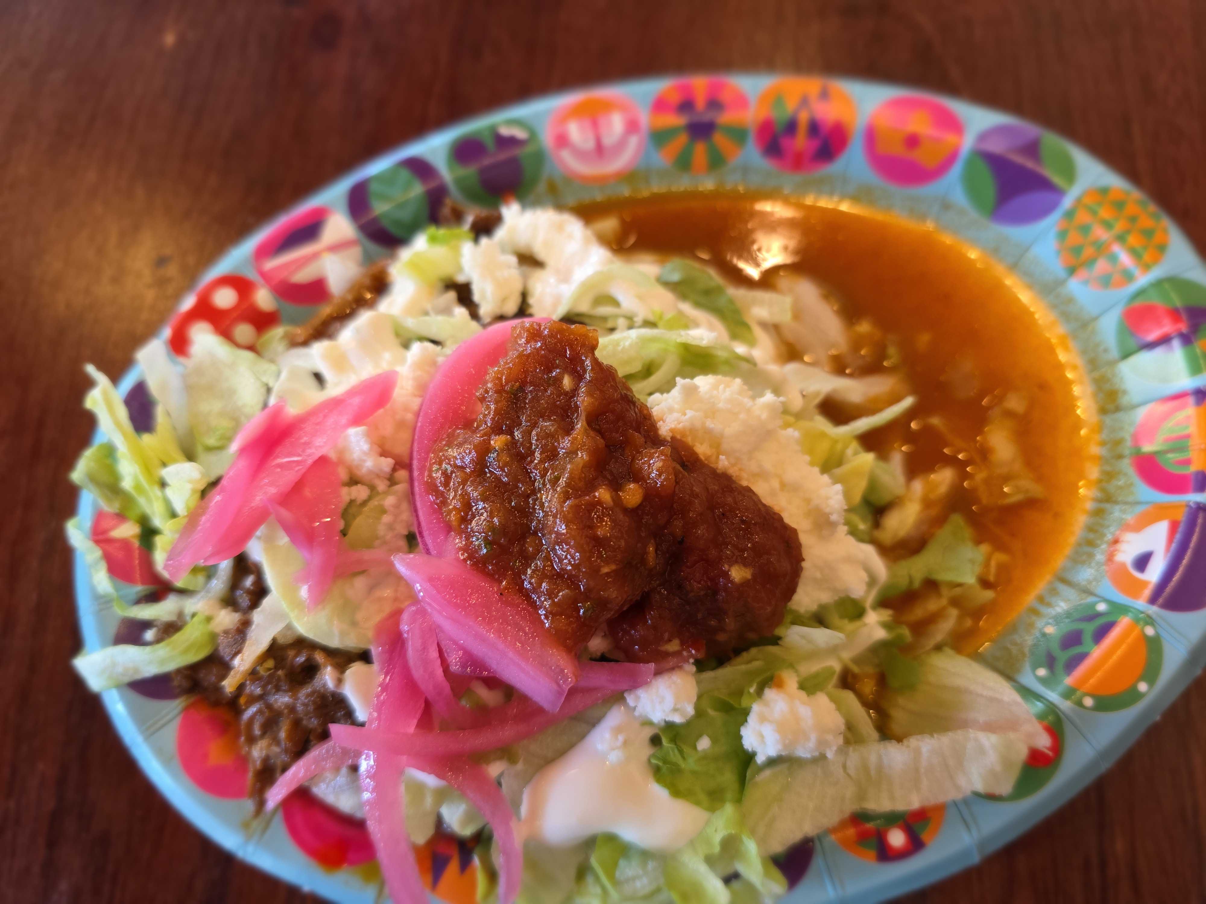 A colorful plate from Cozy Cone Motel with lettuce, pickled onions, cheese, sauce, and sauced meat on a wooden table.