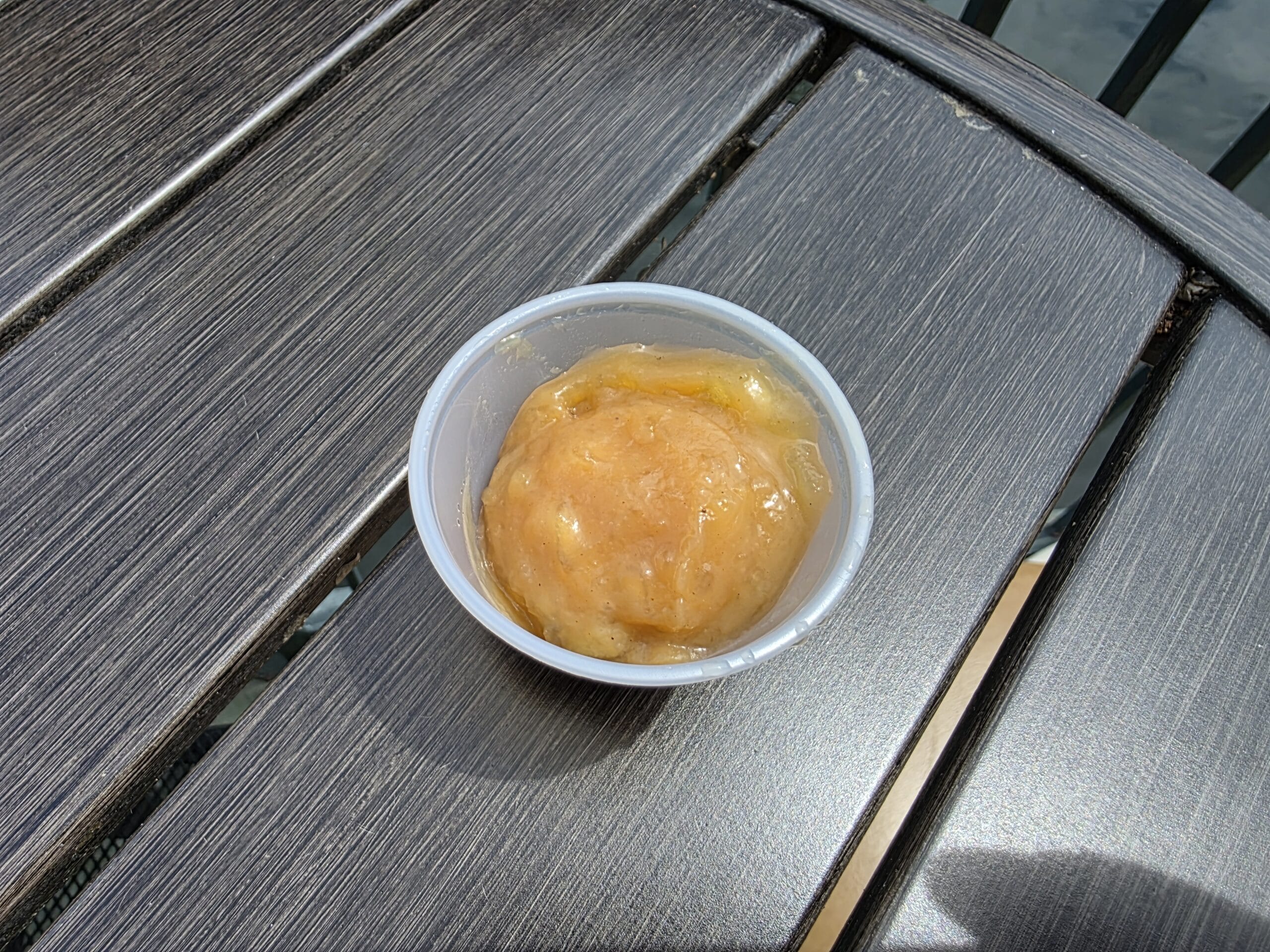 A small plastic cup of brown applesauce sits on a dark wooden table, perfect for dipping sauces at Disneyland.