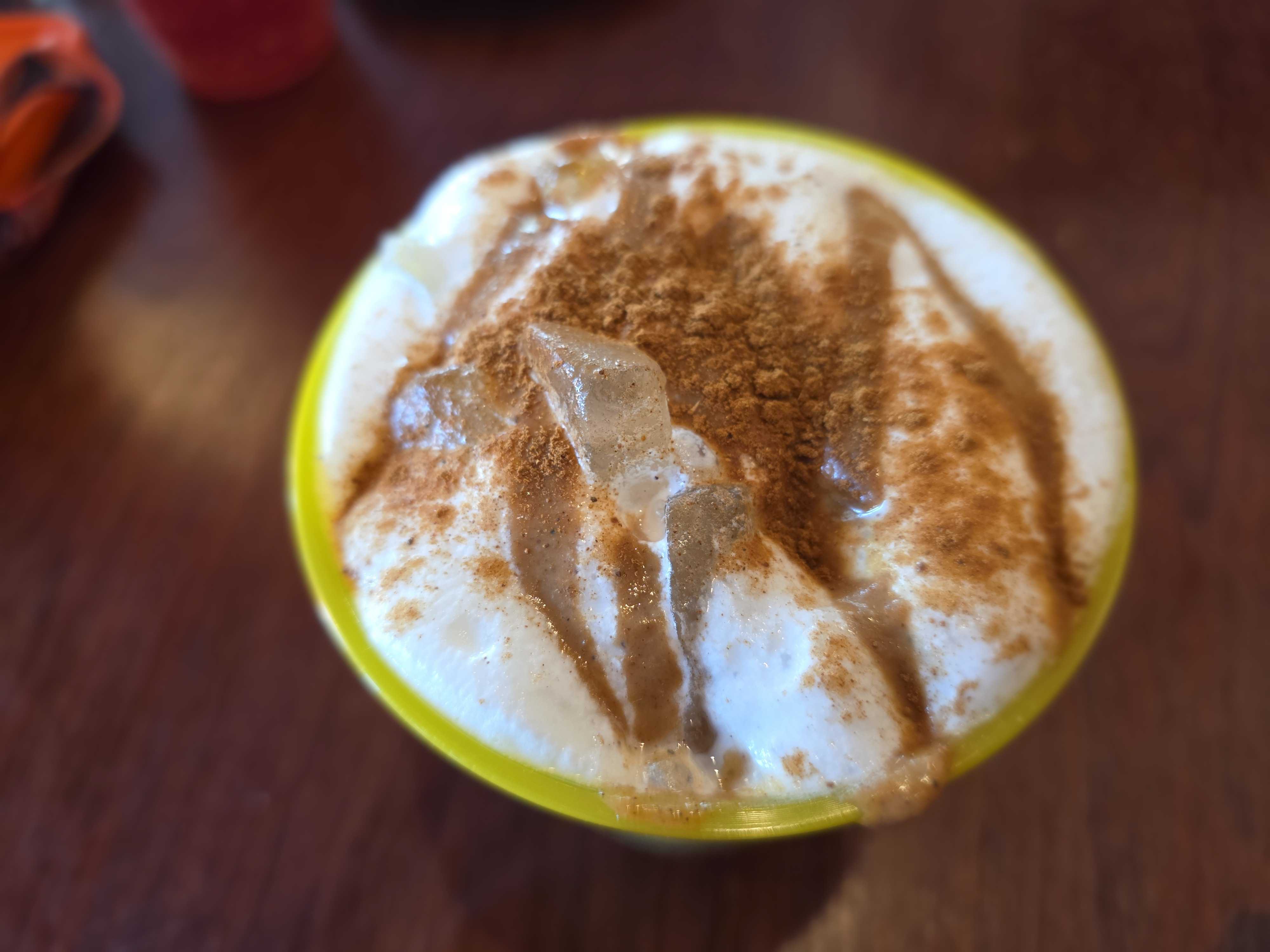 A close-up of a creamy dessert at Cozy Cone Motel, topped with cinnamon and ice cubes in a yellow bowl on a wooden table.