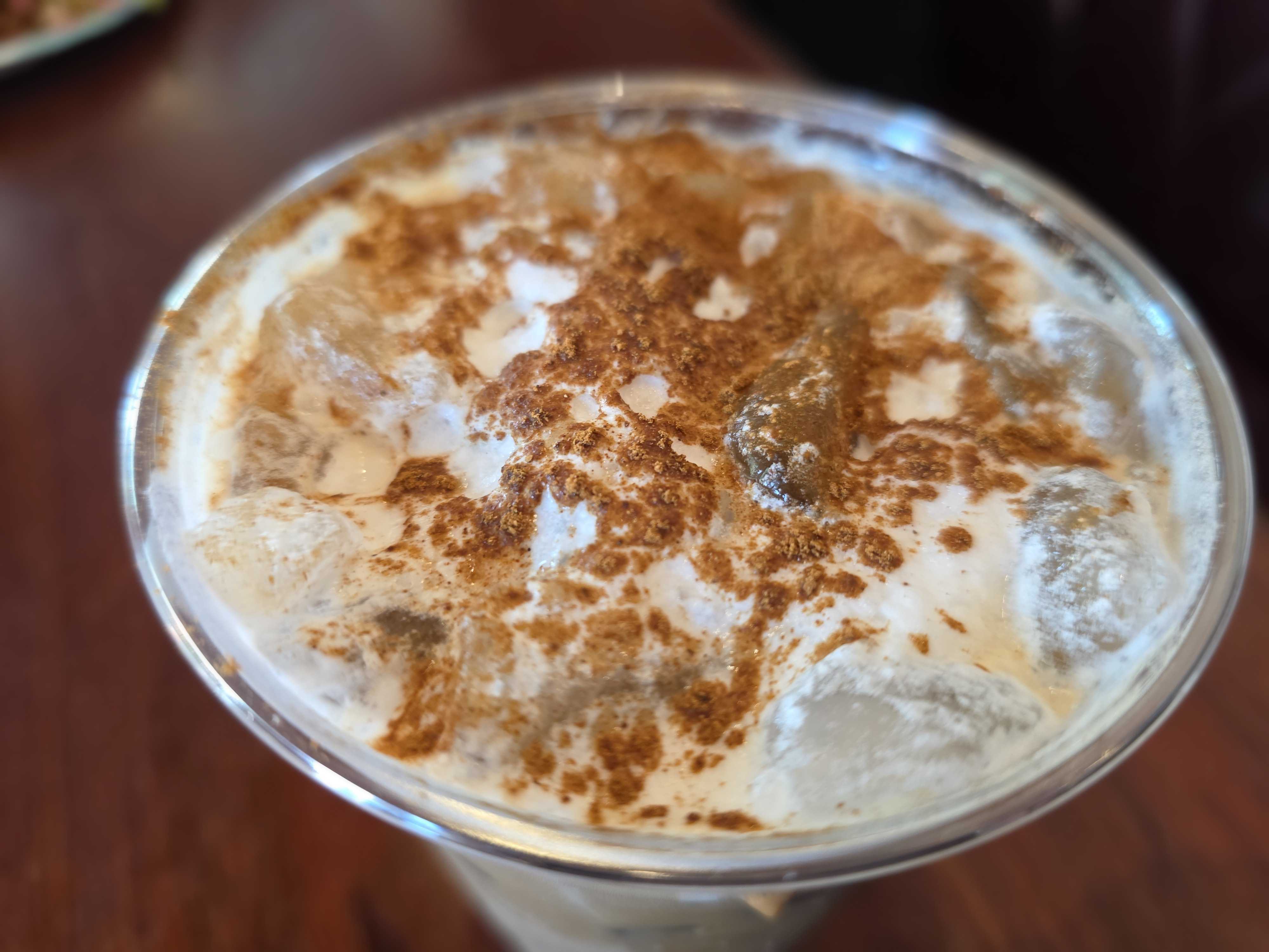 Close-up of an iced coffee topped with cinnamon at Cozy Cone Motel, served in a clear plastic cup.