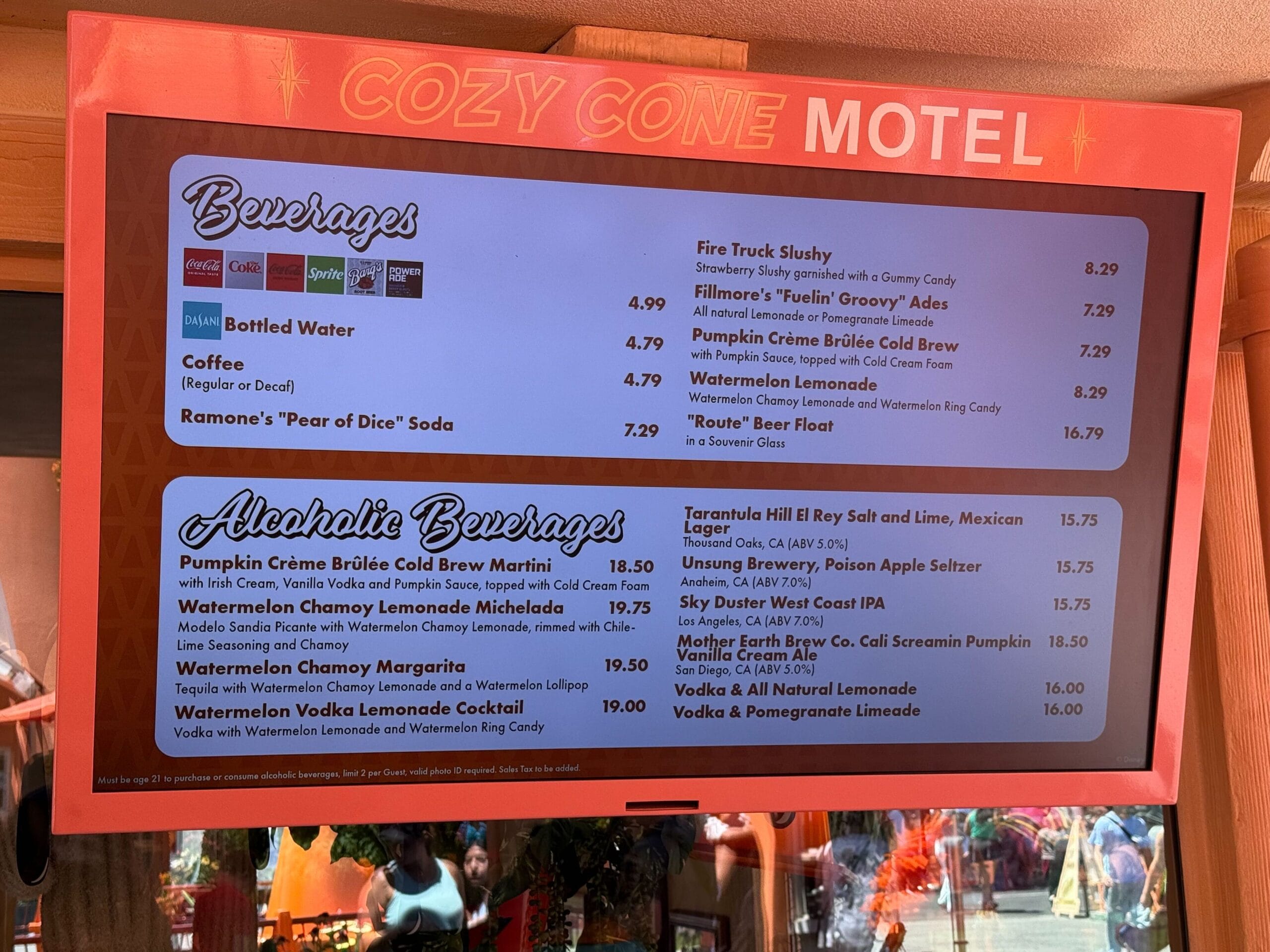 Menu board at Cozy Cone Motel listing beverages, alcoholic drinks, and prices, with a festive orange motel border at the top.