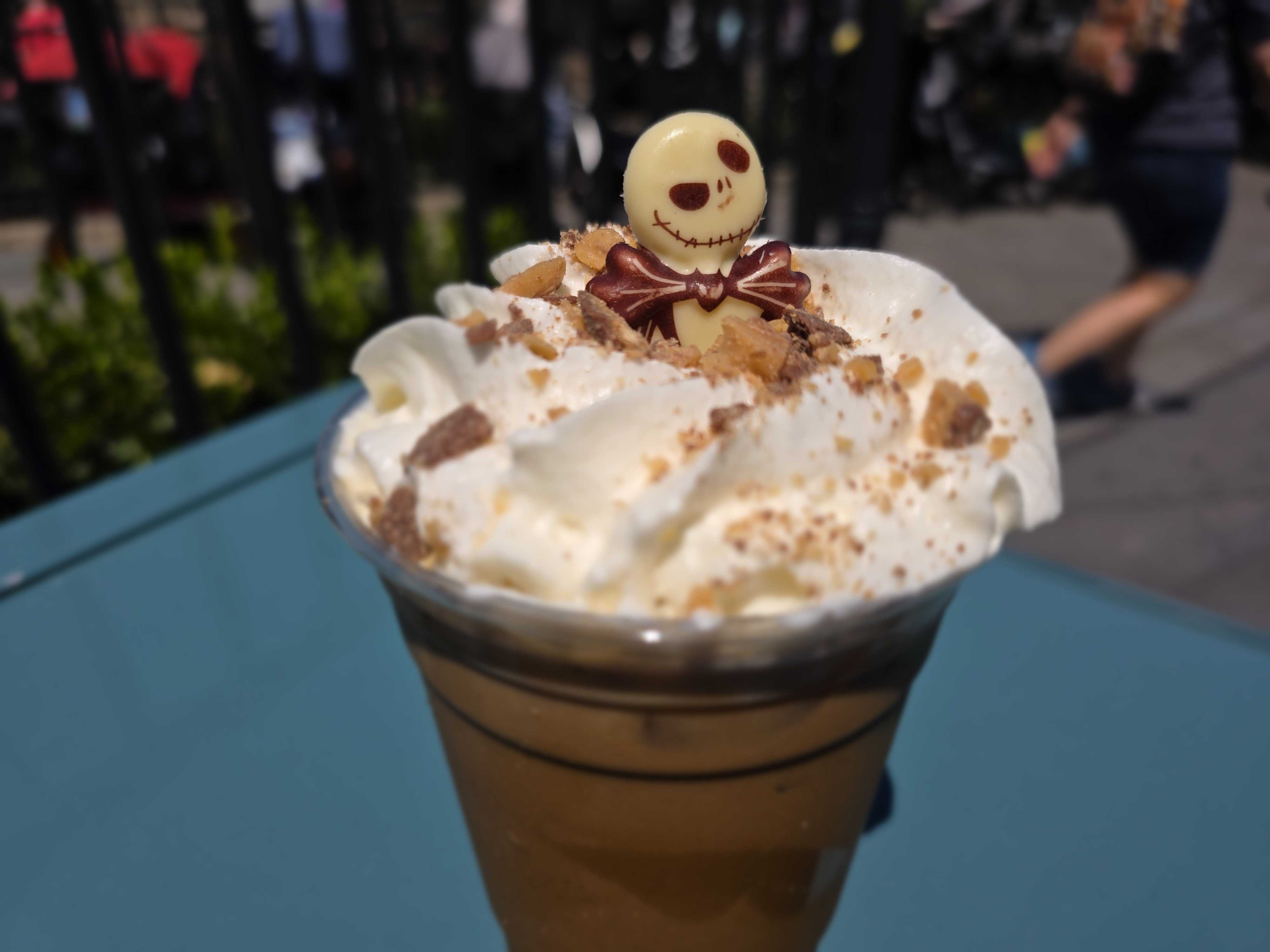Iced Pumpkin Cold Brew topped with whipped cream, crushed nuts, and a Jack Skellington white chocolate decoration.