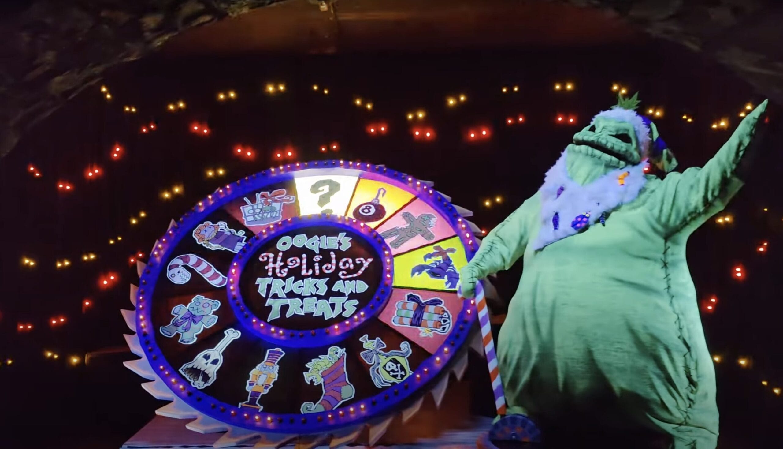 Green character by a colorful spinning wheel, like an Oogie Boogie animatronic from Haunted Mansion Holiday, with festive lights.