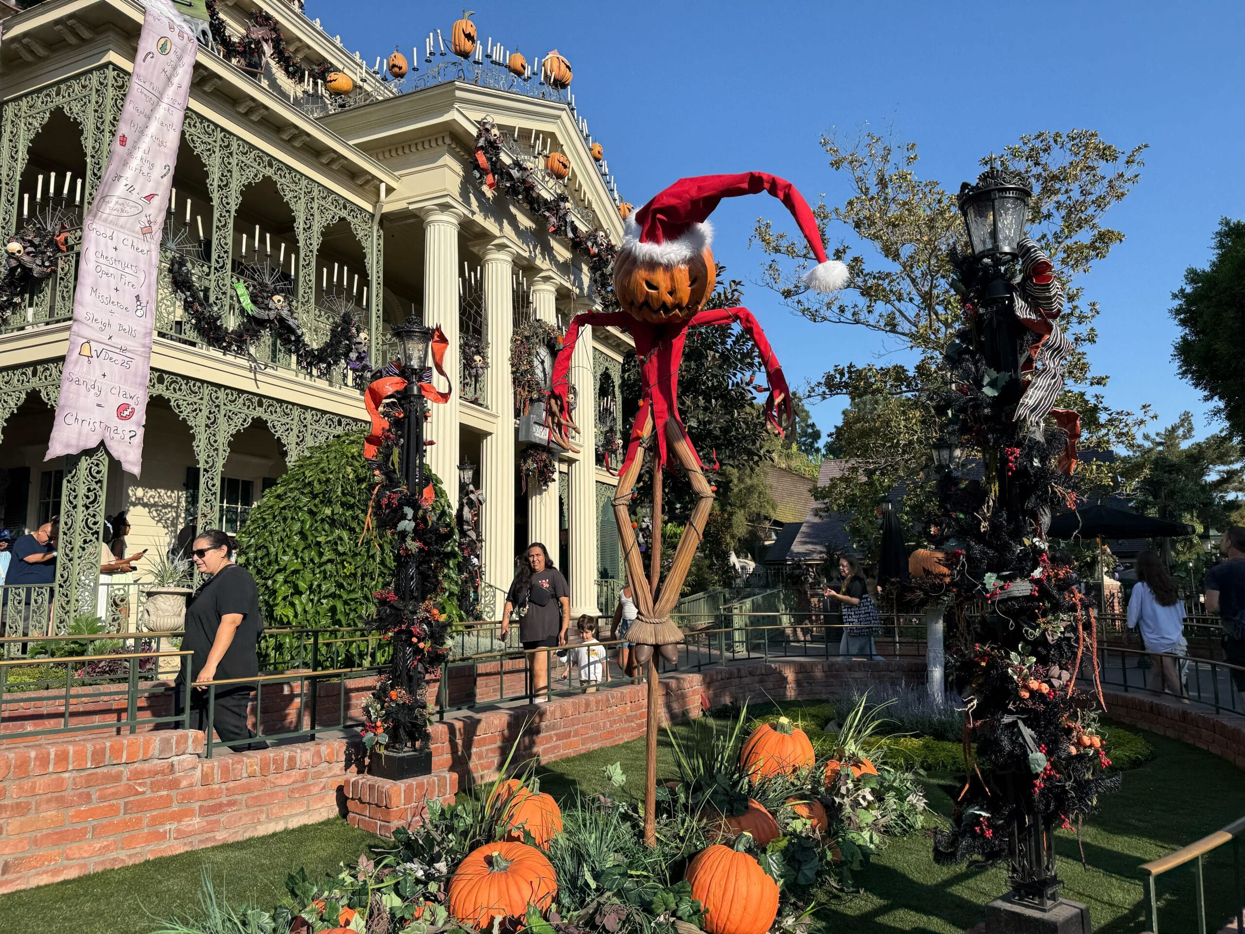 Halloween 2025: Haunted Mansion Holiday decor with pumpkins, Jack Skellington scarecrow, and people strolling by.