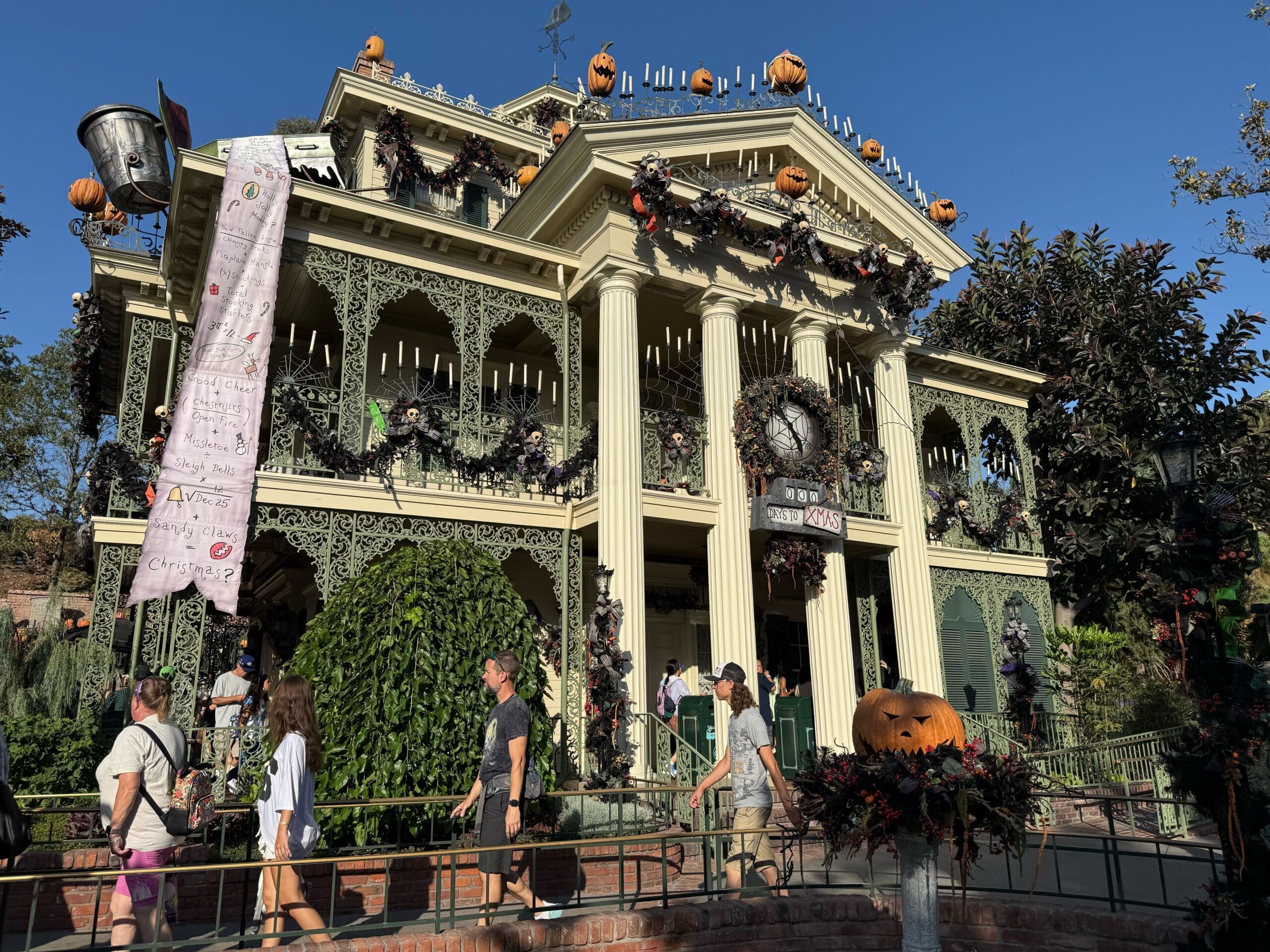 Haunted Mansion Holiday adorned with pumpkins and garlands, people strolling by on a sunny Halloween 2025 day.